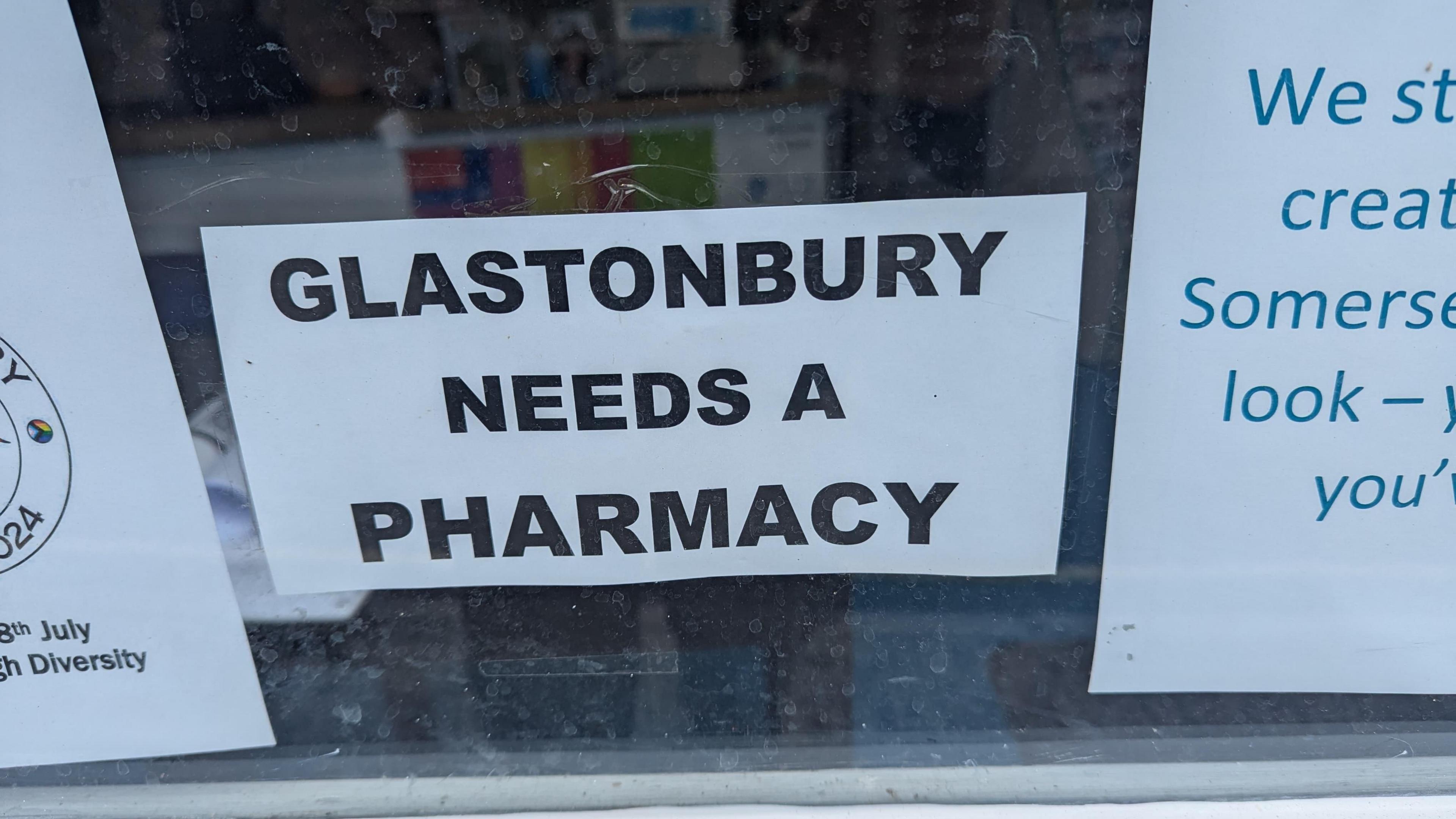 A sign in a window reading 'Glastonbury needs a pharmacy'.