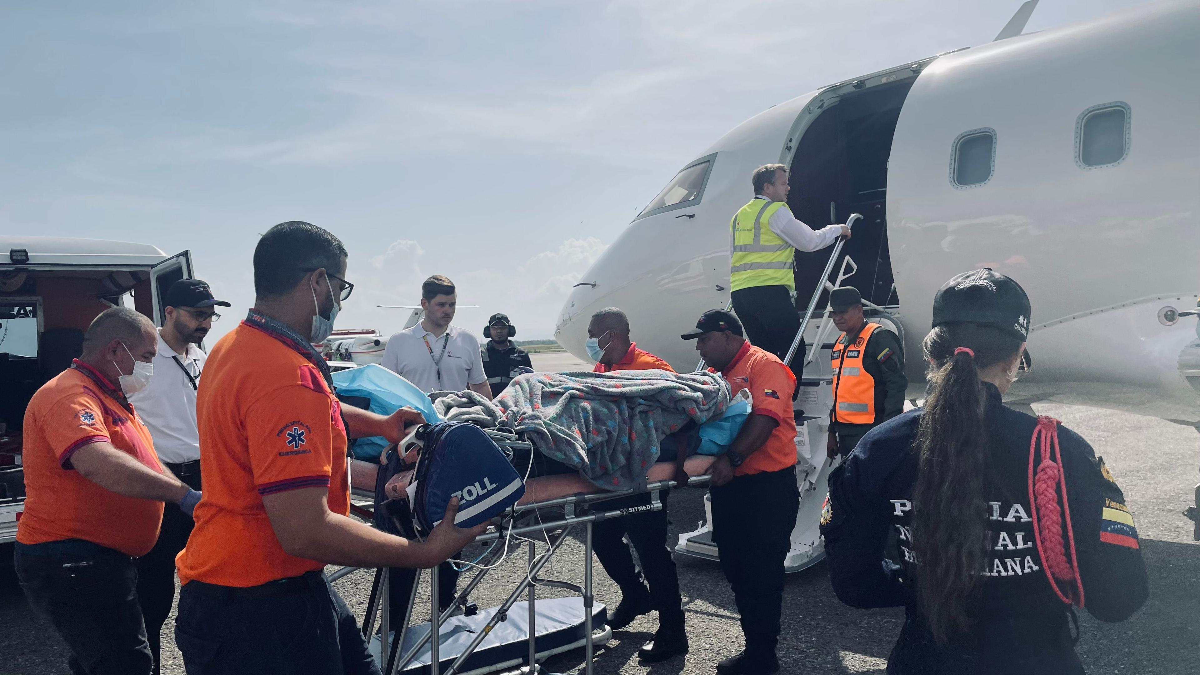 A group of medicas are pushing a stretcher with seb on (covered in a blanket) towards a small plane.