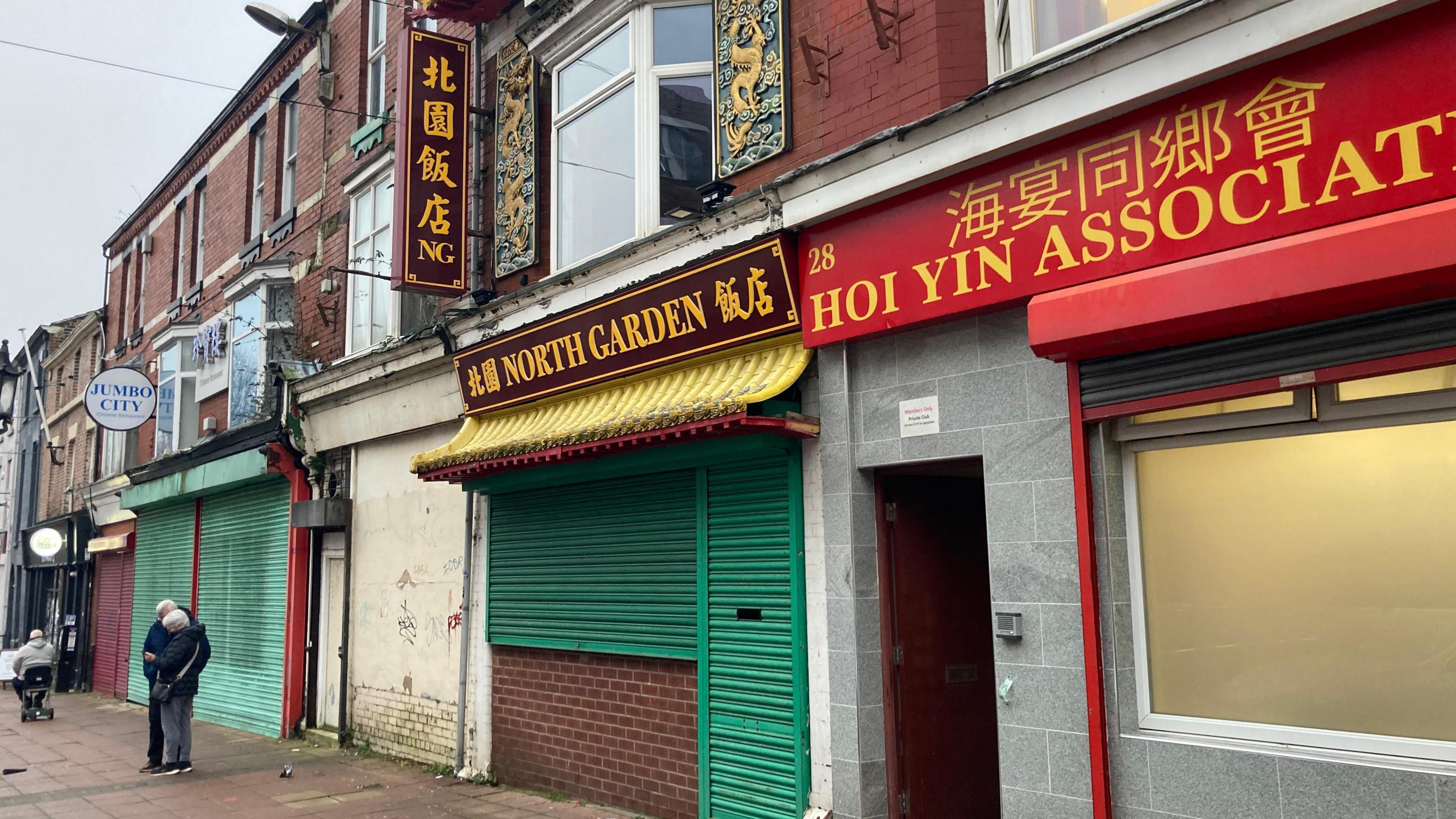 A row of terraced buildings with shops at the bottom, with shutters up on the front of the shops