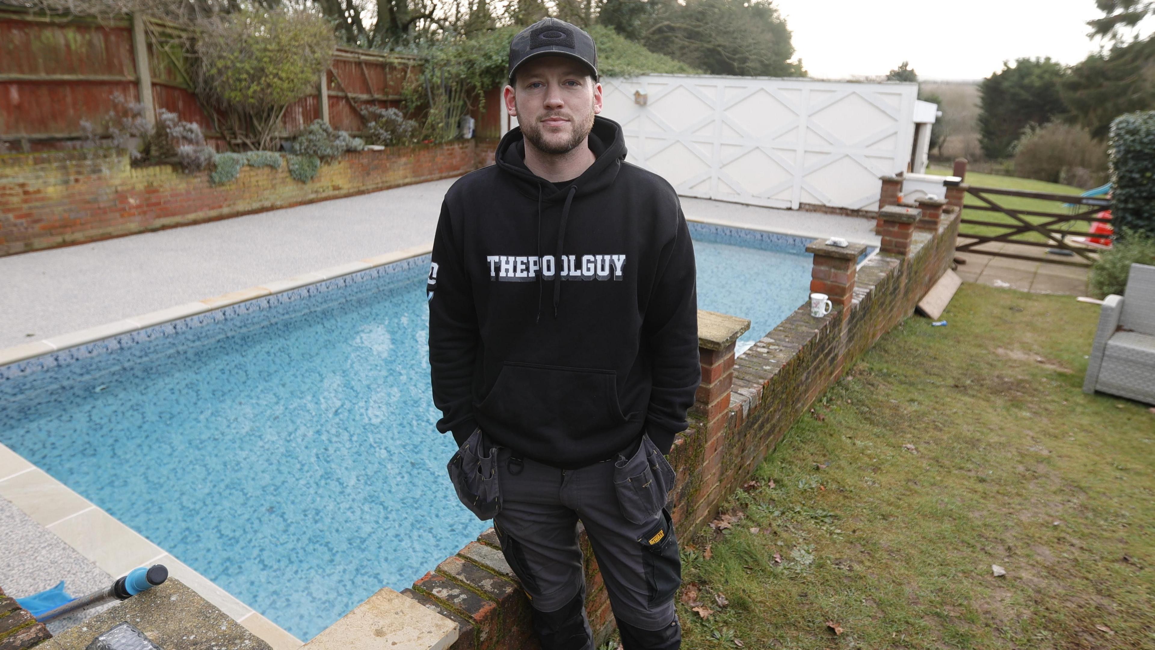 Miles Laflin is stood in front of a swimming pool. He is wearing all black and smiling at the camera.