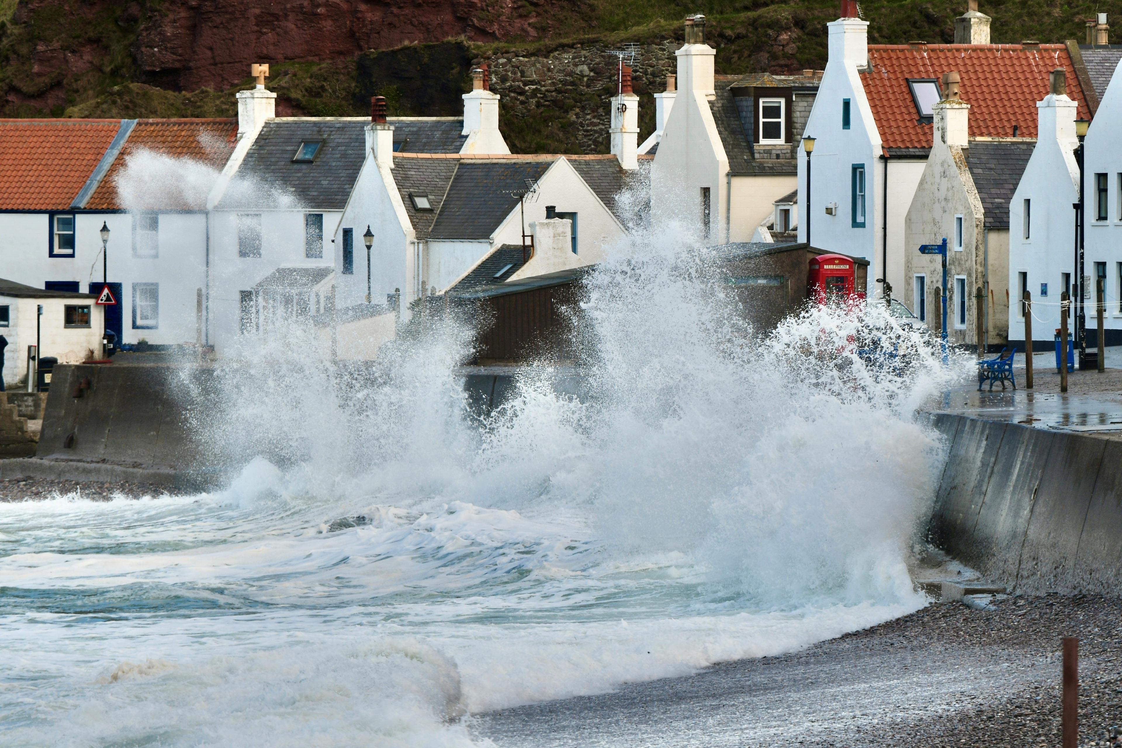 Waves crash into a protective wall next to a row of houses