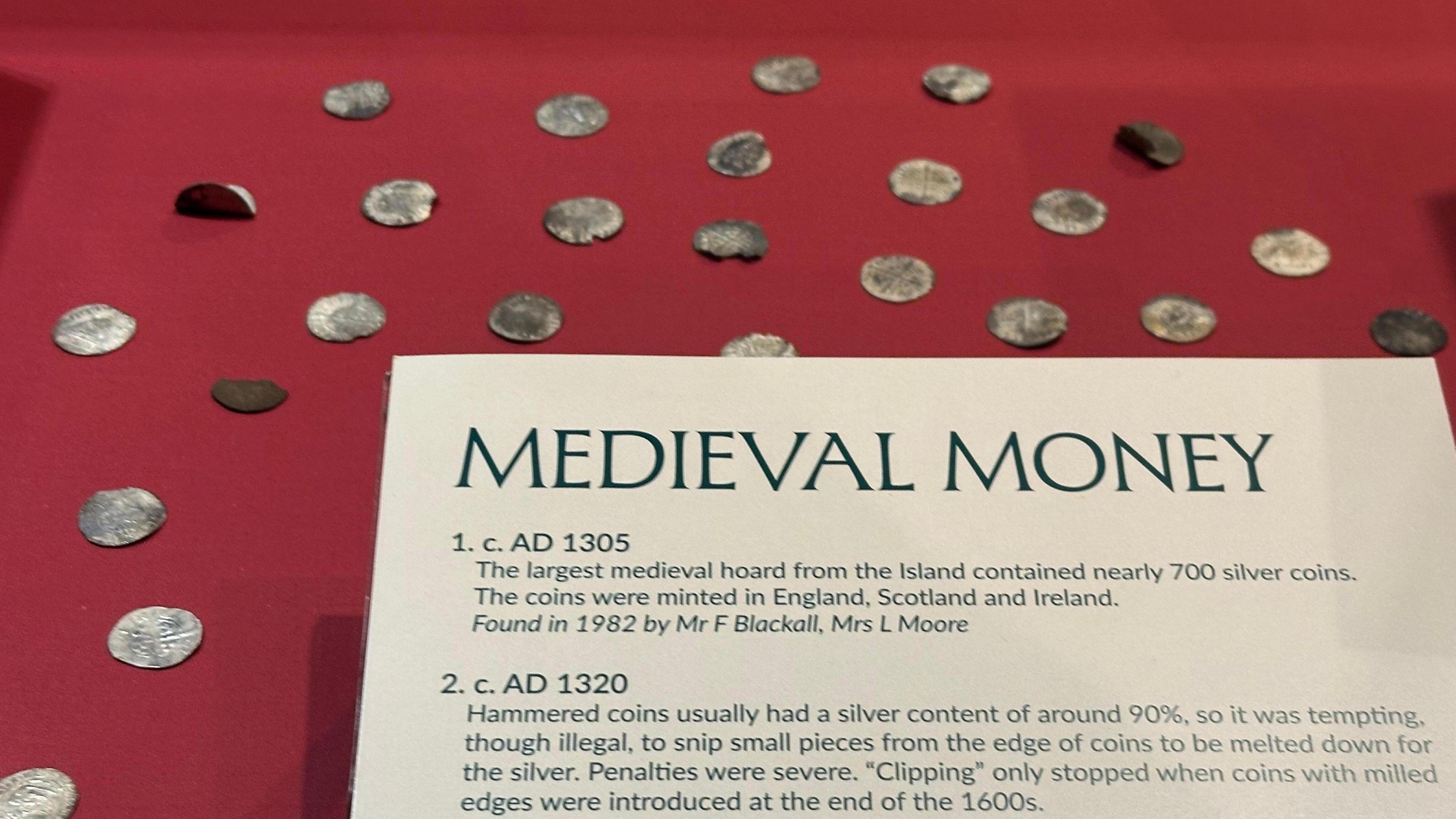 Silver coins laid out on a red surface with a card with Medieval Money and information about the coins in the fore.