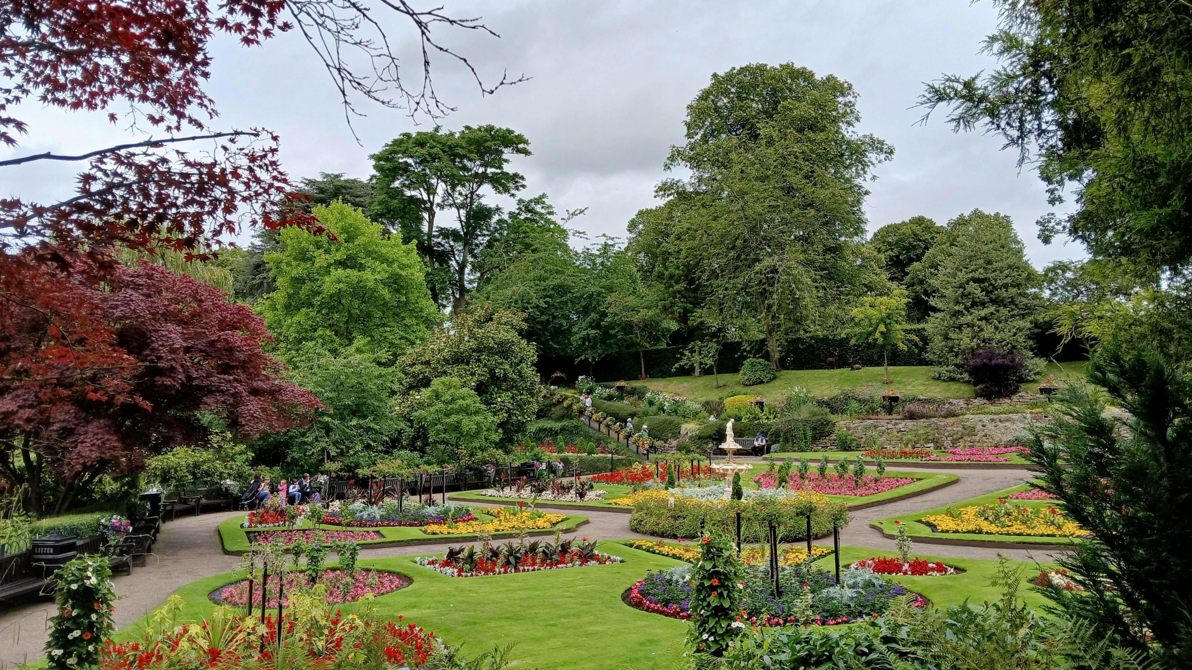 A wide shot of the Dingle formal gardens at the main park in Shrewsbury, the Quarry. Beds are laid out among trees, lawns and paths with flowers in a variety of colours