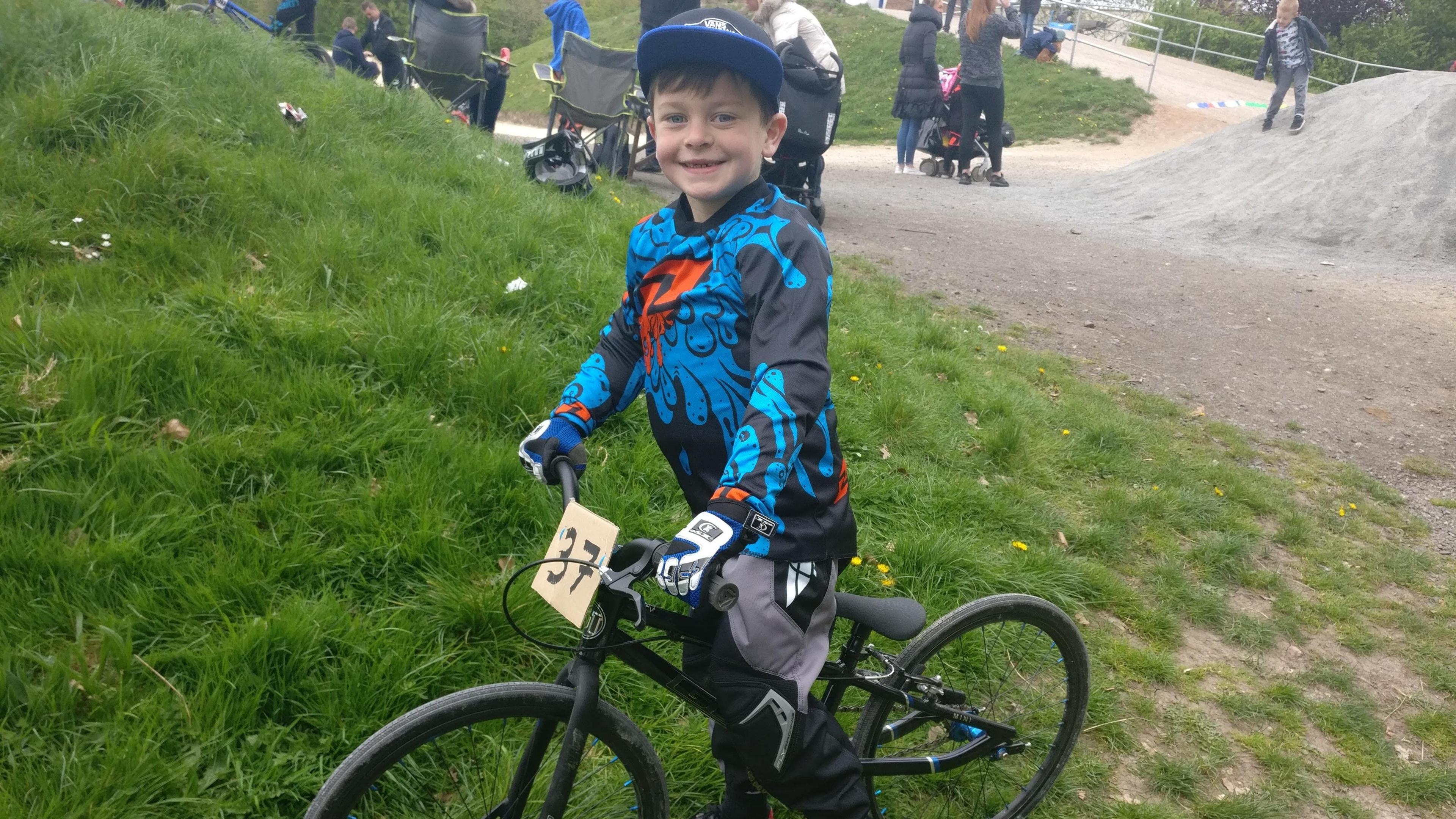 A boy wearing a blue and black jumper sits on a BMX bike on the grass. 