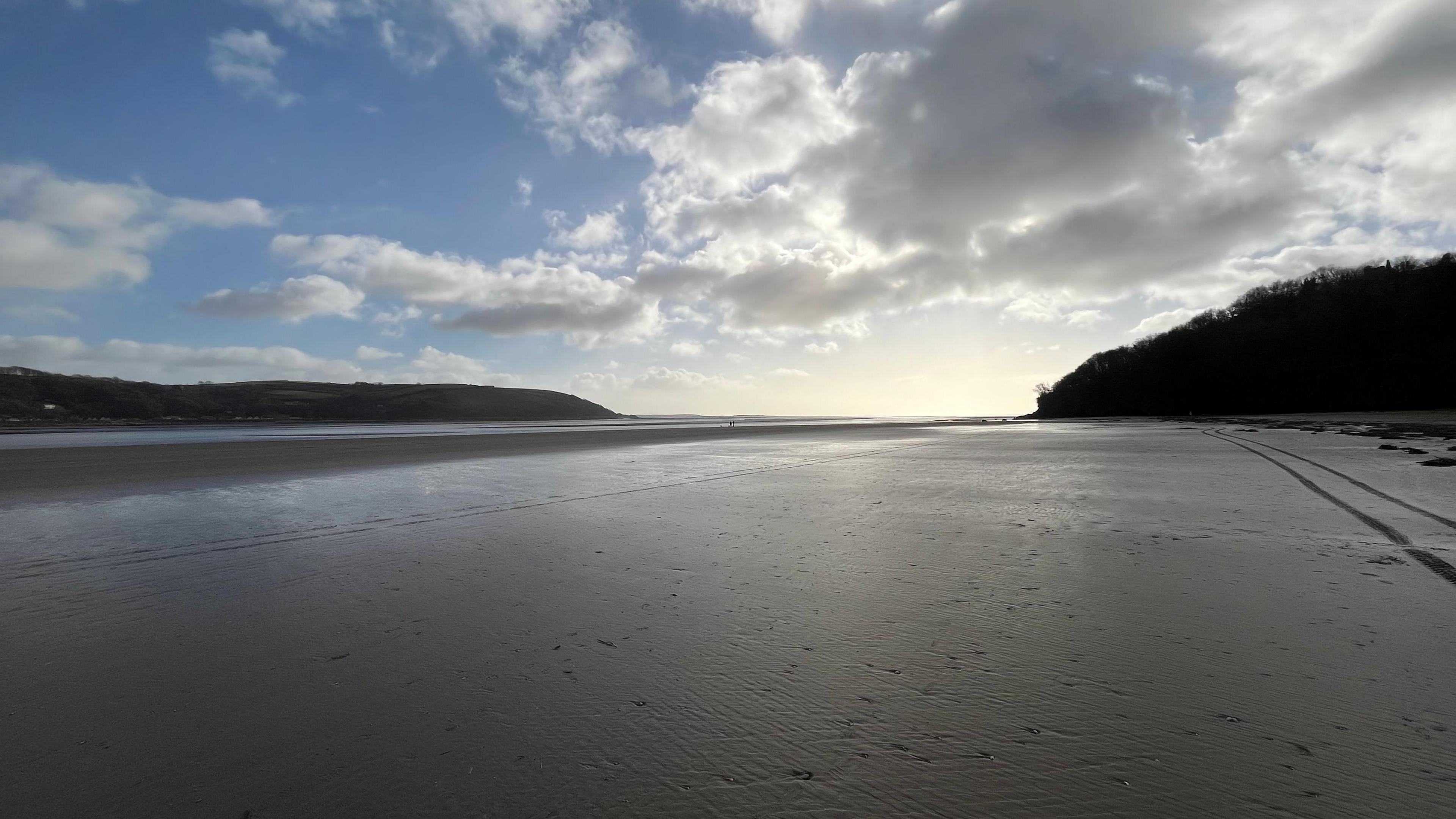 An empty sandy beach at sunset with hills in the background