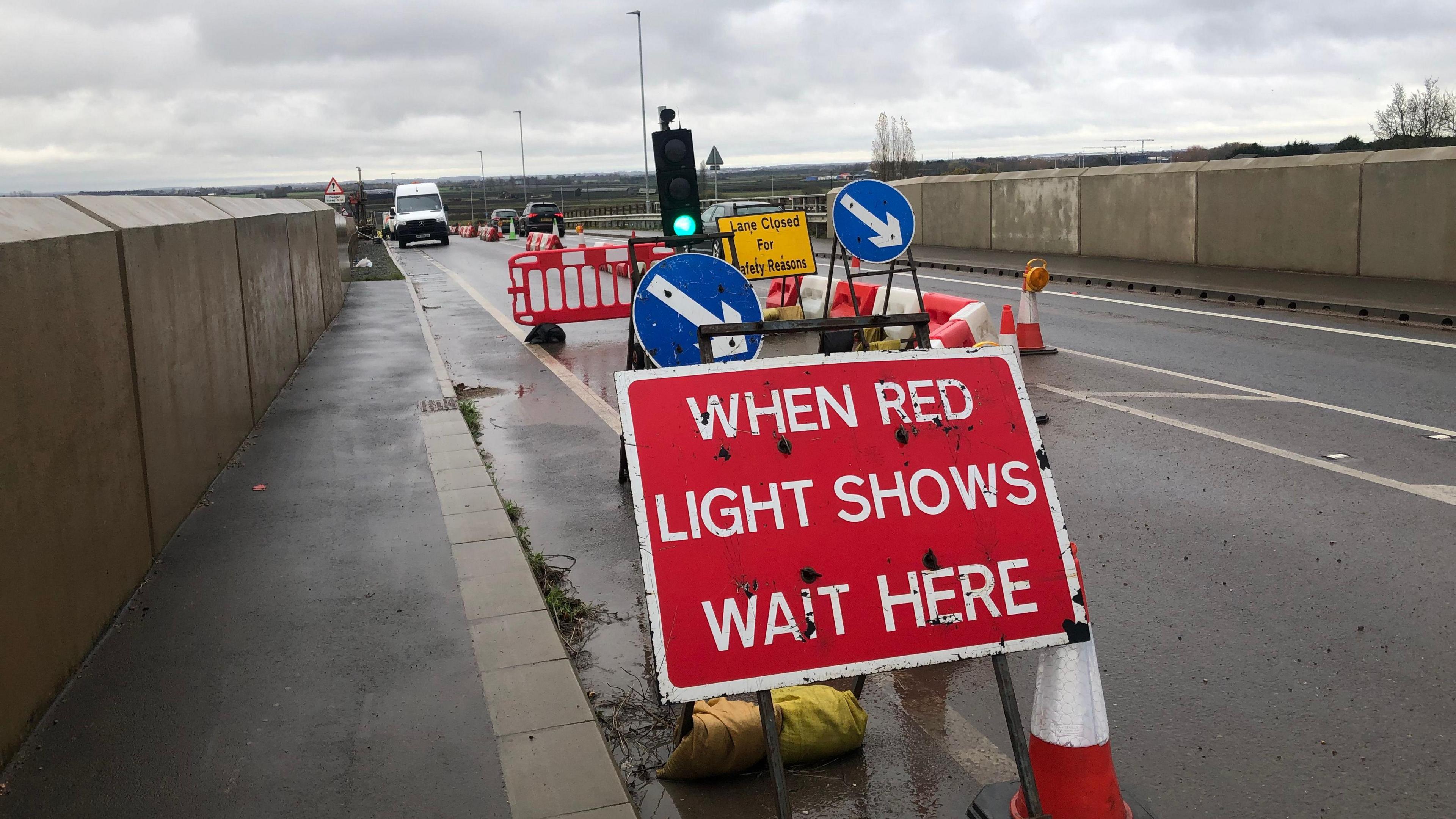 A picture of a bridge with temporary traffic lights. At the front is a red and white sign that reads "When Red Light Shows Wait Here". 