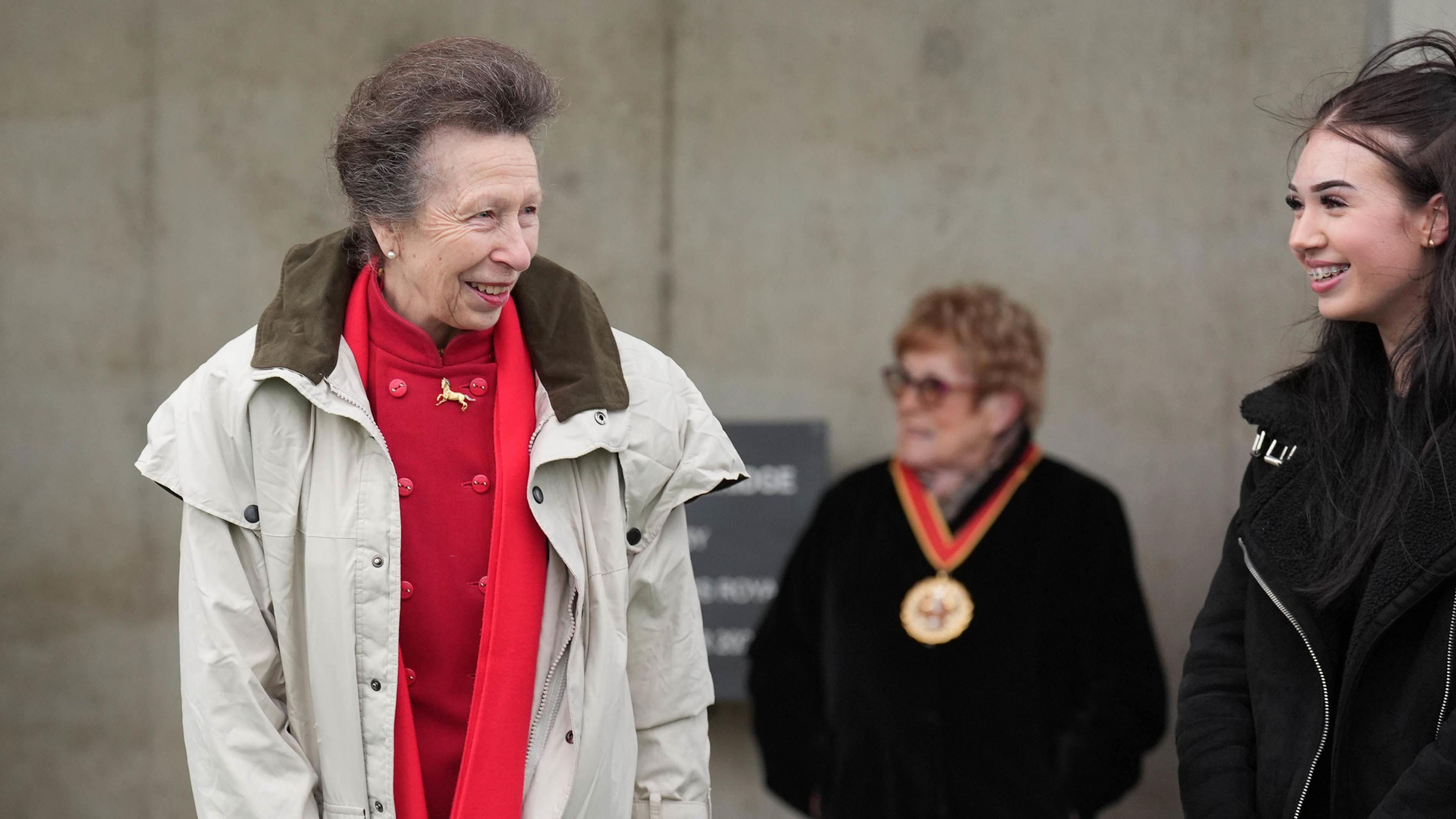 Princess Anne talks with a young person on the bridge. They are both smiling while looking at one another. 