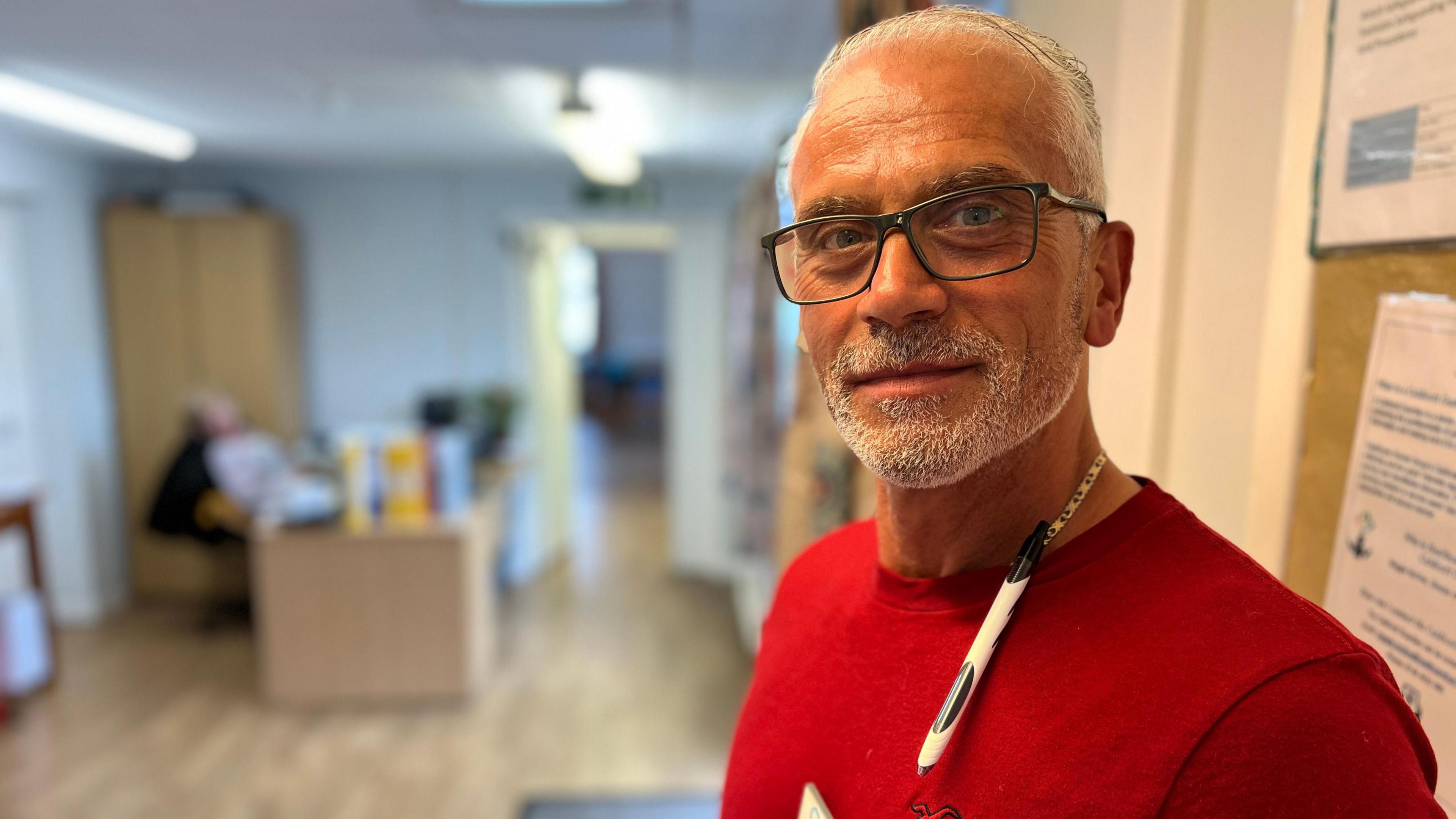 Nik Psarras in a red T-shirt, looking at the camera