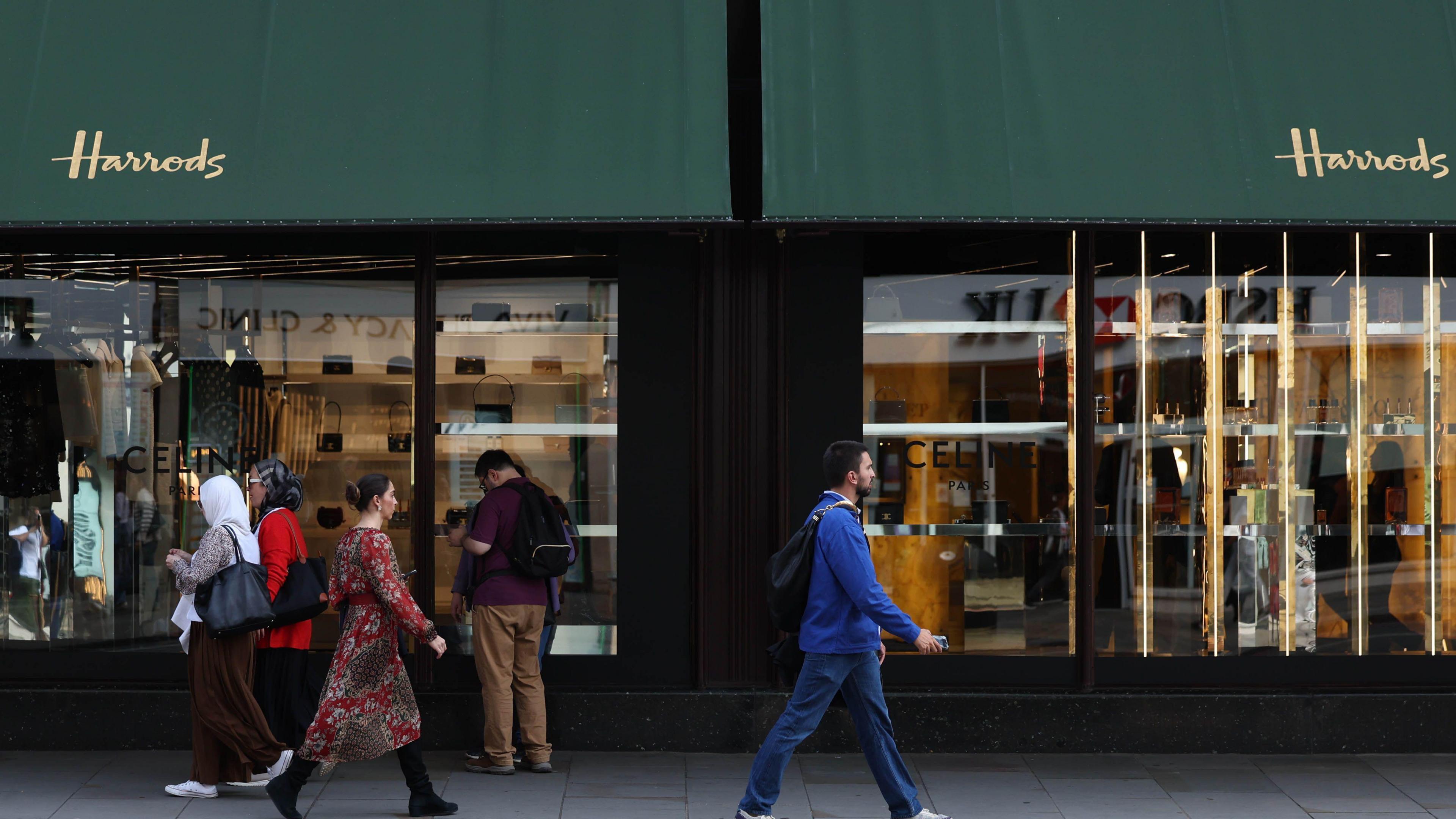 Pedestrians walk past the windows of Harrods in Knightsbridge, London. Five people can be seen outside the store. 