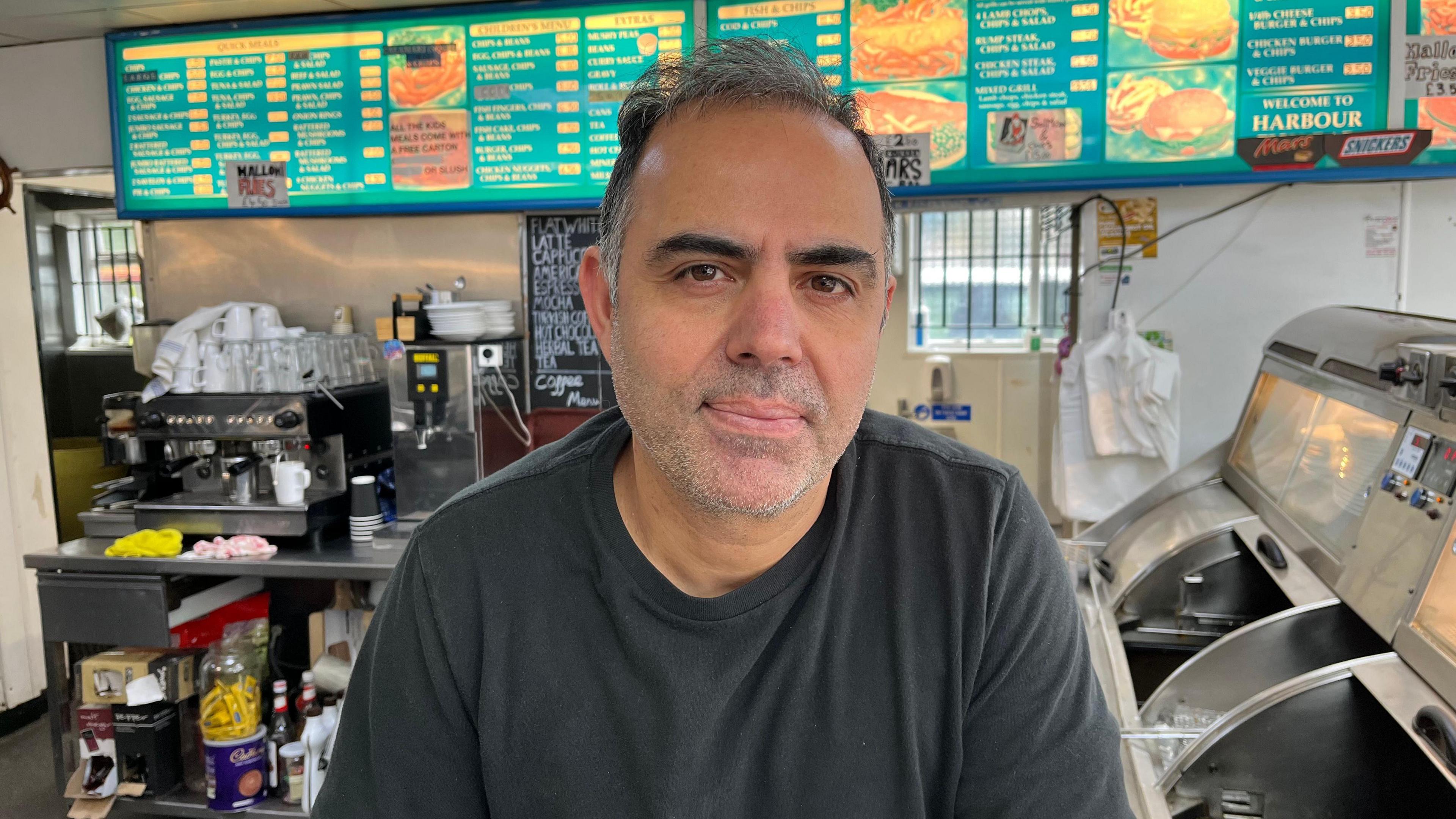 Murat Karakartal from behind the counter in his fish and chip shop in Folkestone, he wears a dark coloured t-shirt