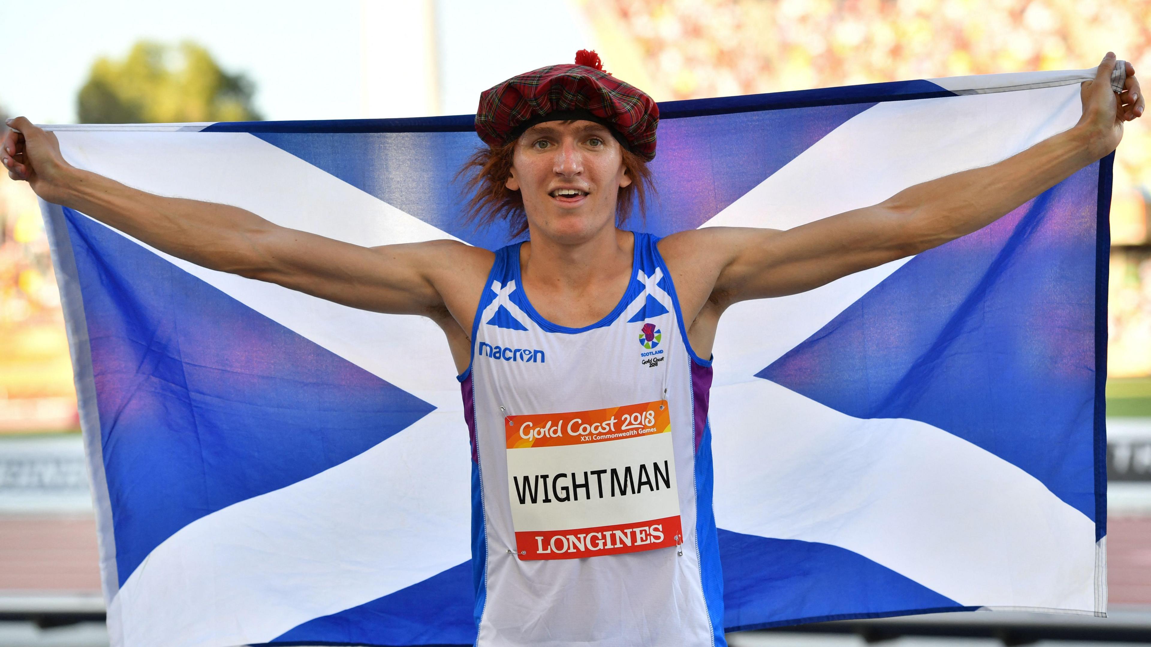 Jake Wightman holds up a Scotland flag while wearing a See You Jimmy hat after success on the athletics track.
