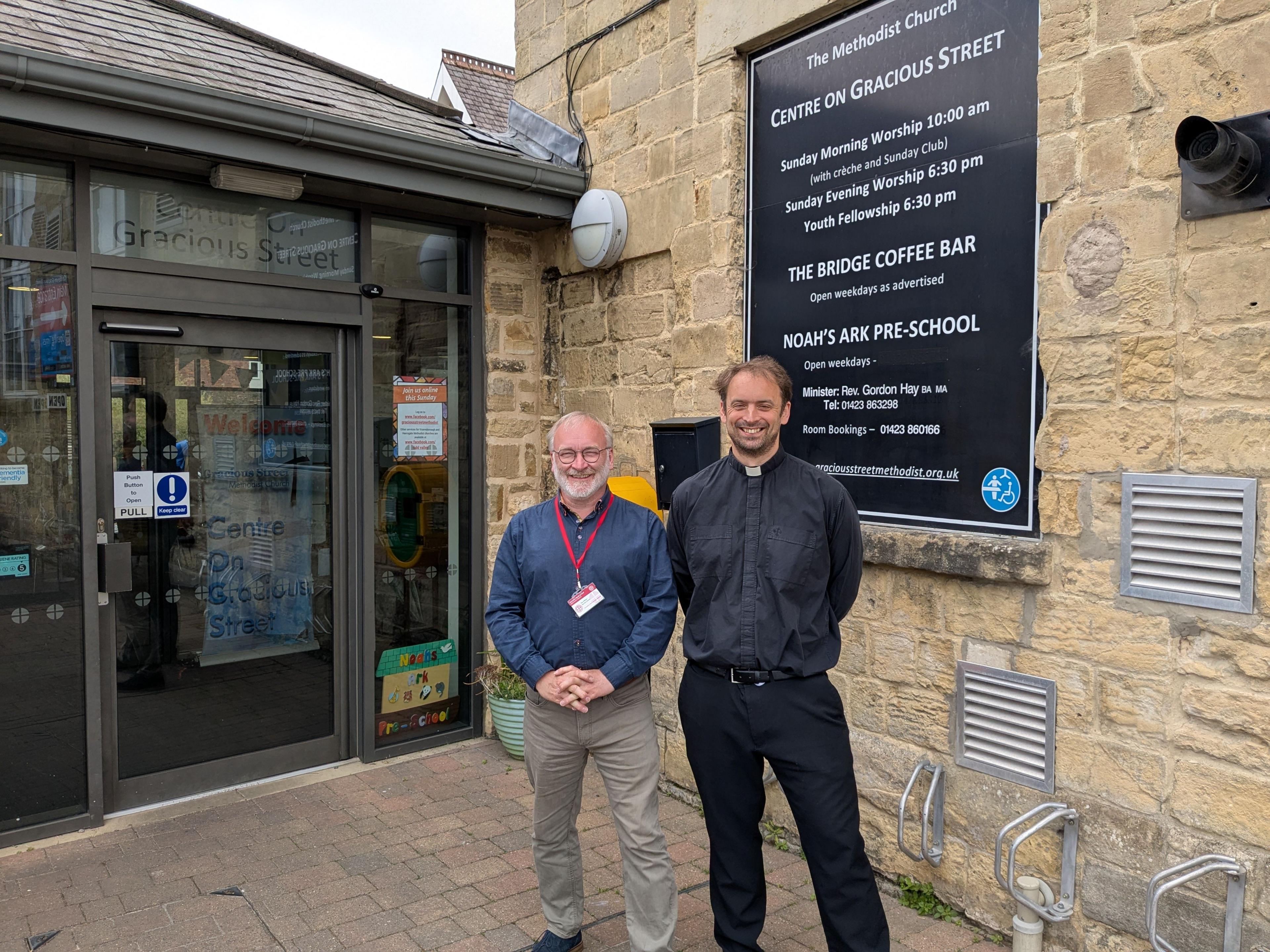Tim O'Brien, Net Zero Officer for the Yorkshire North & East Methodist District - in a long-sleeved dark blue shirt and beige trousers - and the Reverend Gordon Hay - wearing a dog collar and dark trousers - standing outside Gracious Street Methodist Church in Knaresborough