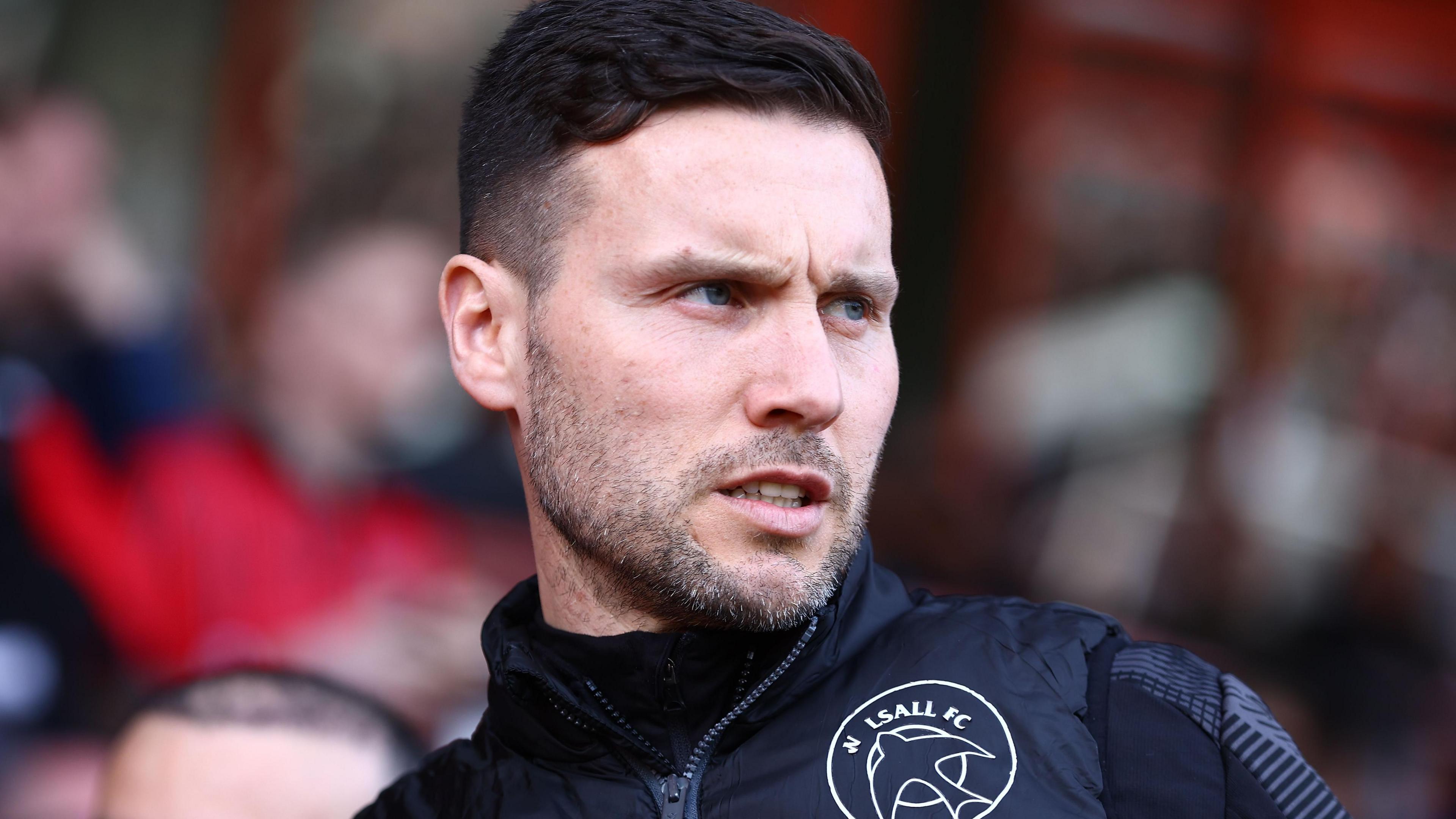 Walsall manager Mat Sadler watching a game, wearing a dark tracksuit