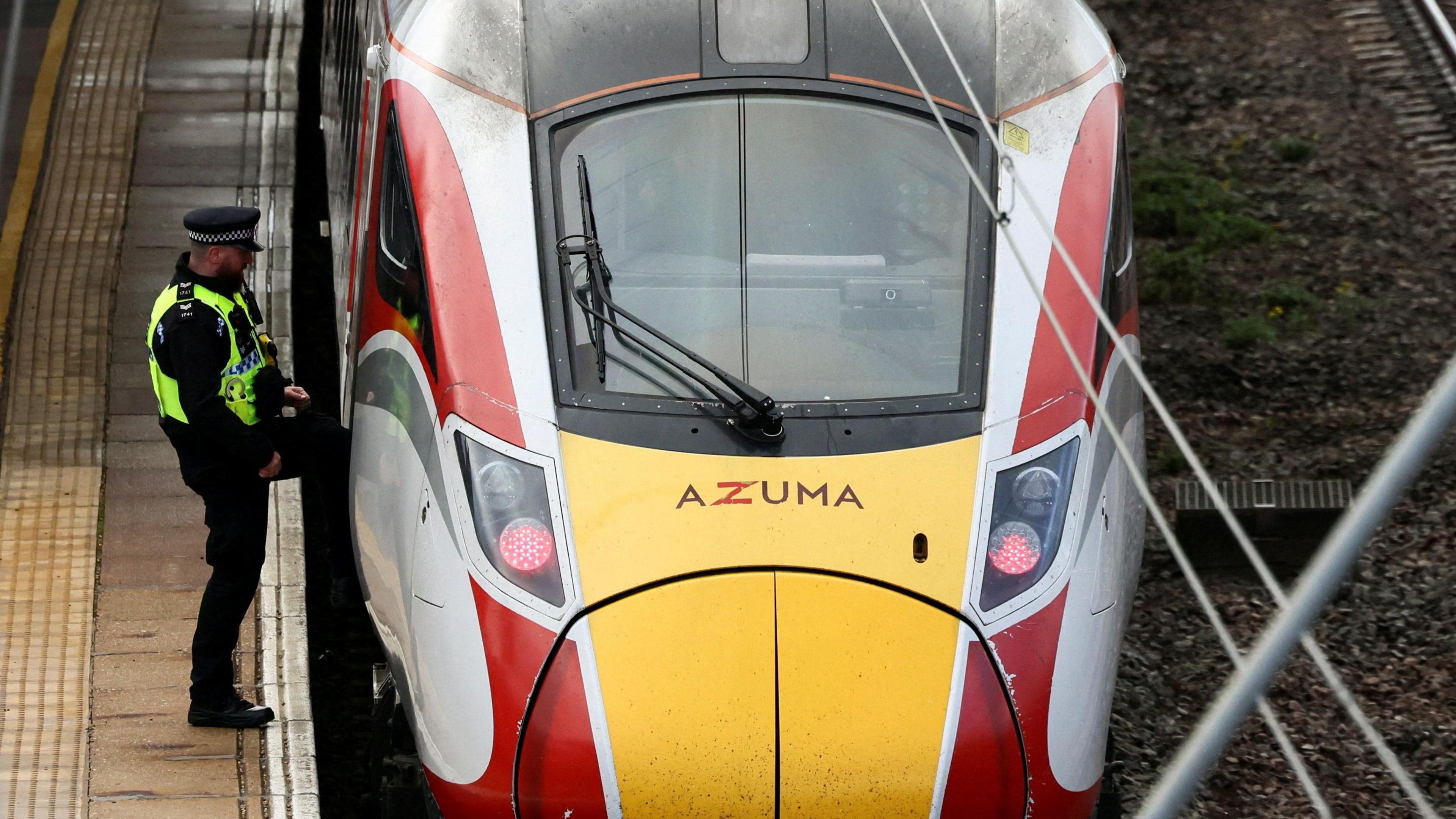 A police officer in a hi-vis jacket over his uniform stepping into the cab of a red, yellow and white train.