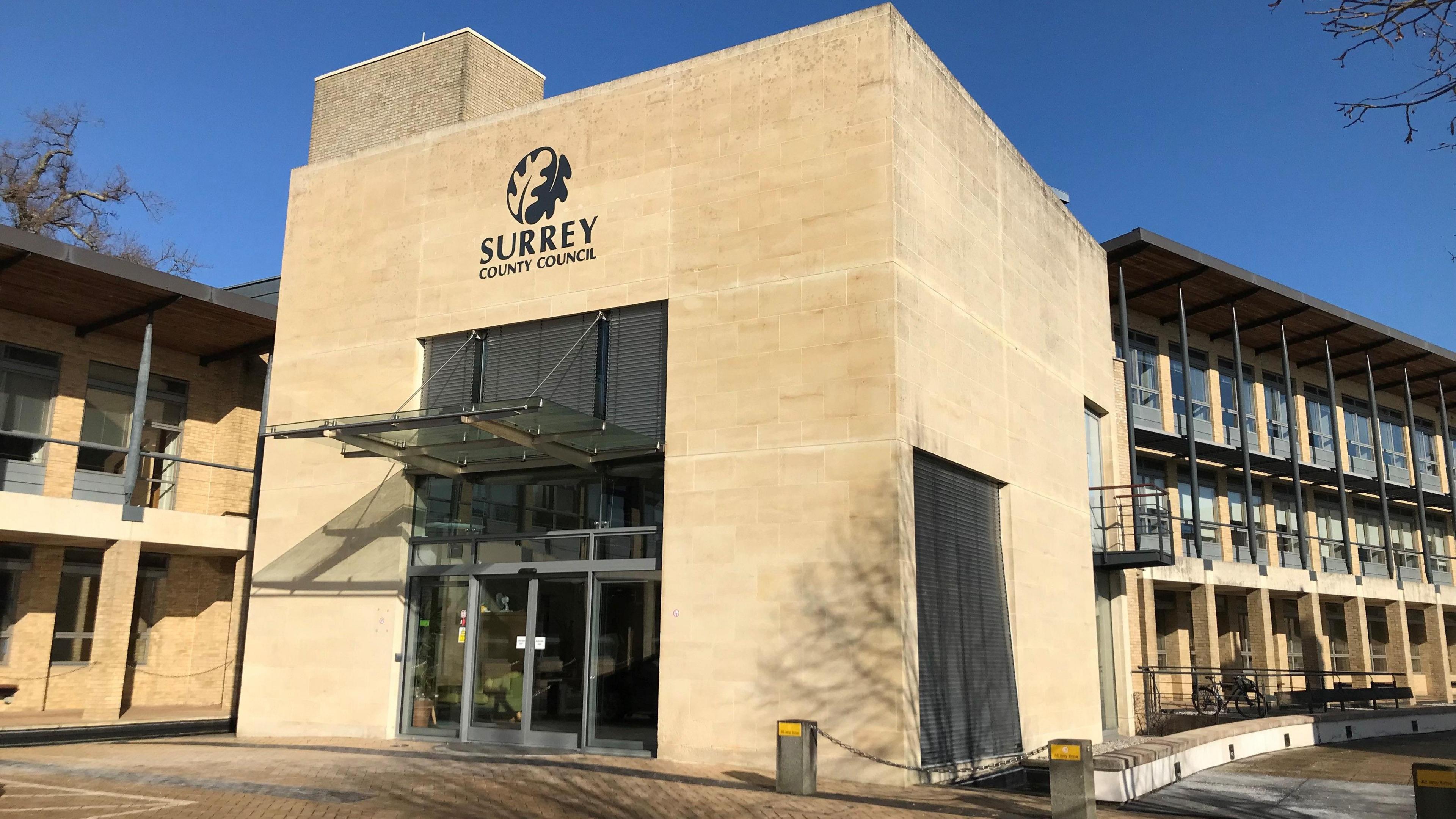 The outside of Surrey County Council's headquarters in Woodhatch Place, Reigate. It is a low buildings made of pale stone and glass