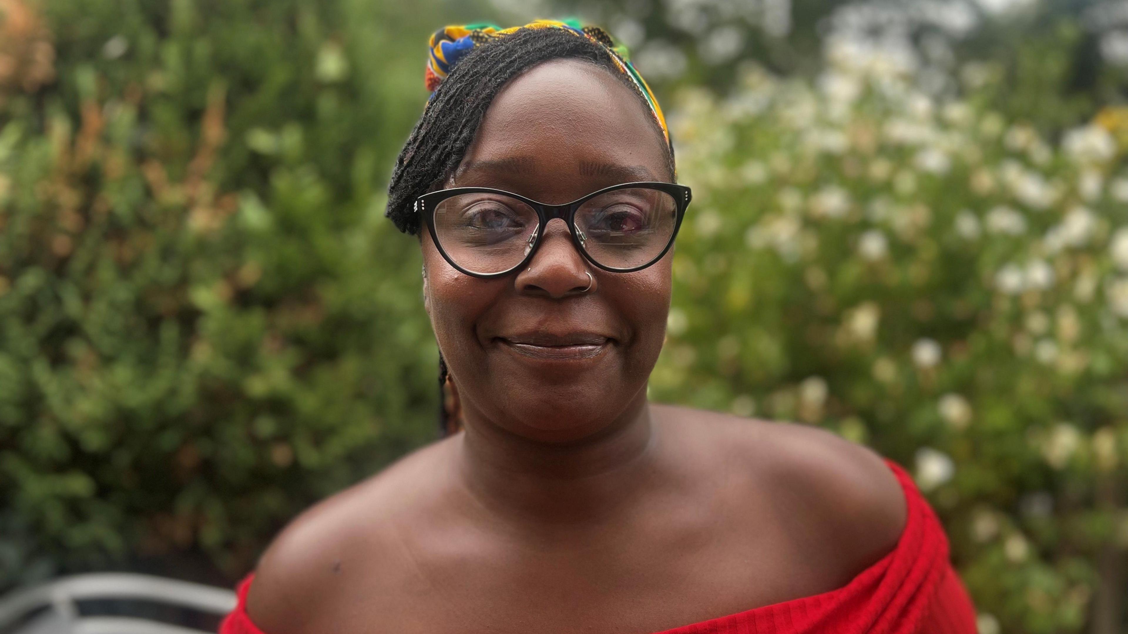 Leasuwanna Griffith, who is wearing black rimmed glasses and a red strapless top and a colourful headscarf in her hair. She is smiling at the camera.