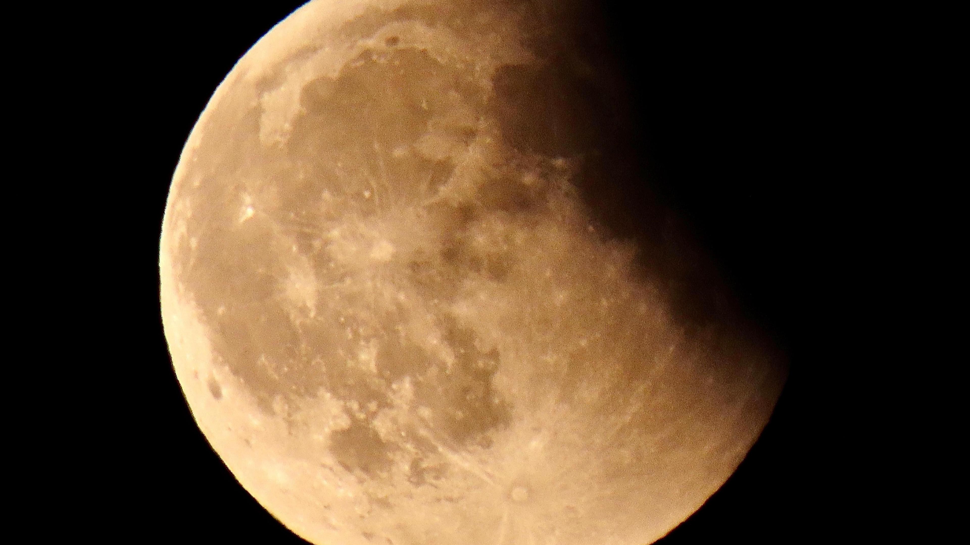 The Moon with a shadow cast across one side of it with the rest in a light yellow colour