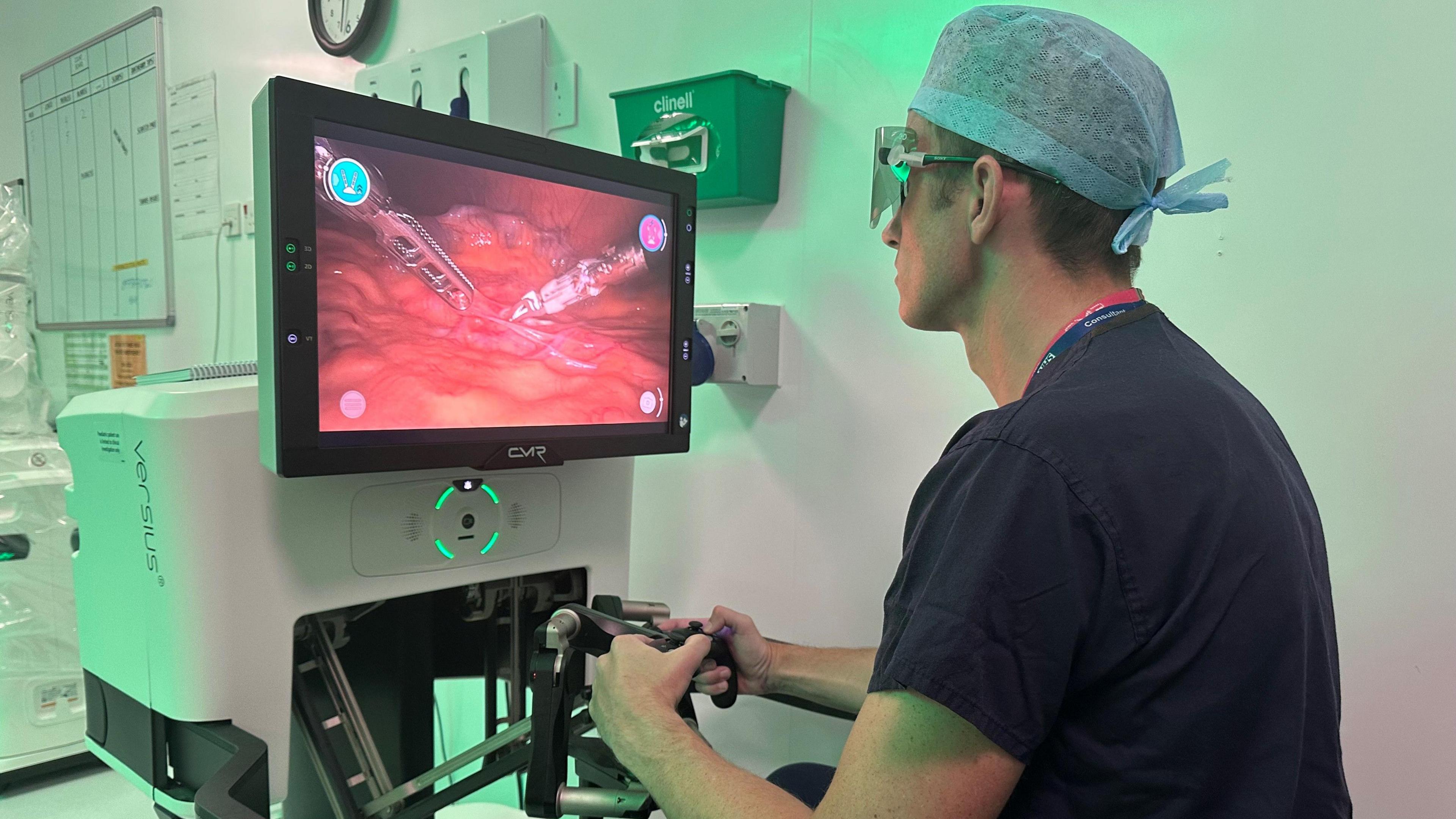 Surgeon Ewan Brownlee operates the Versius robot, watching a patient's internal soft tissue on a screen as he manipulates hand-held controls