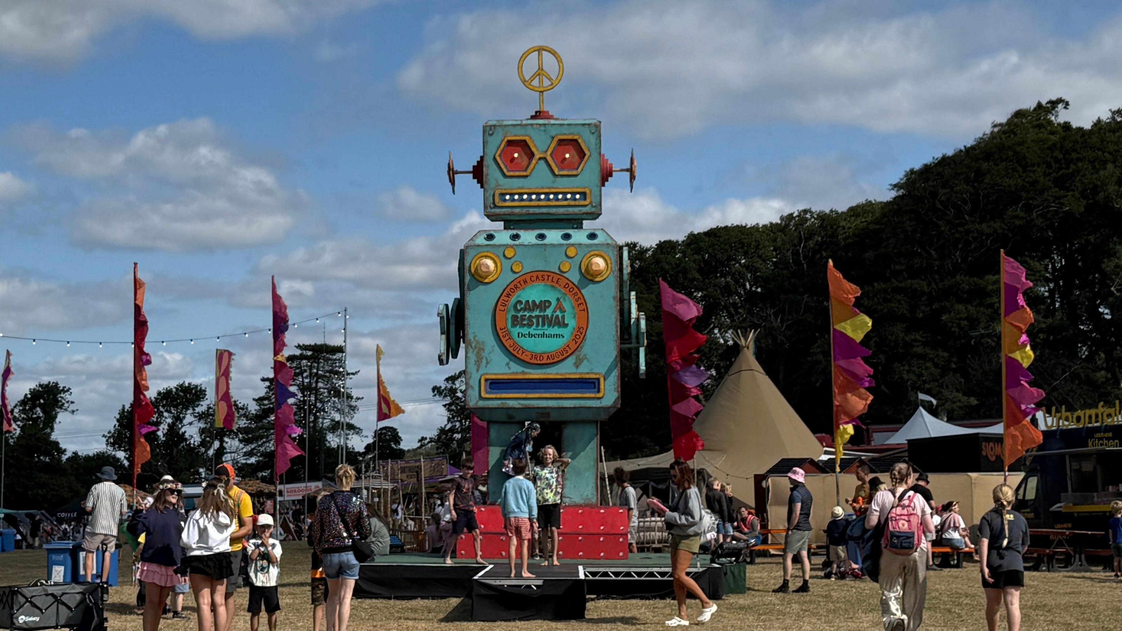 A large blue robot figure with the festival logo on towers over festival-goers and flags.