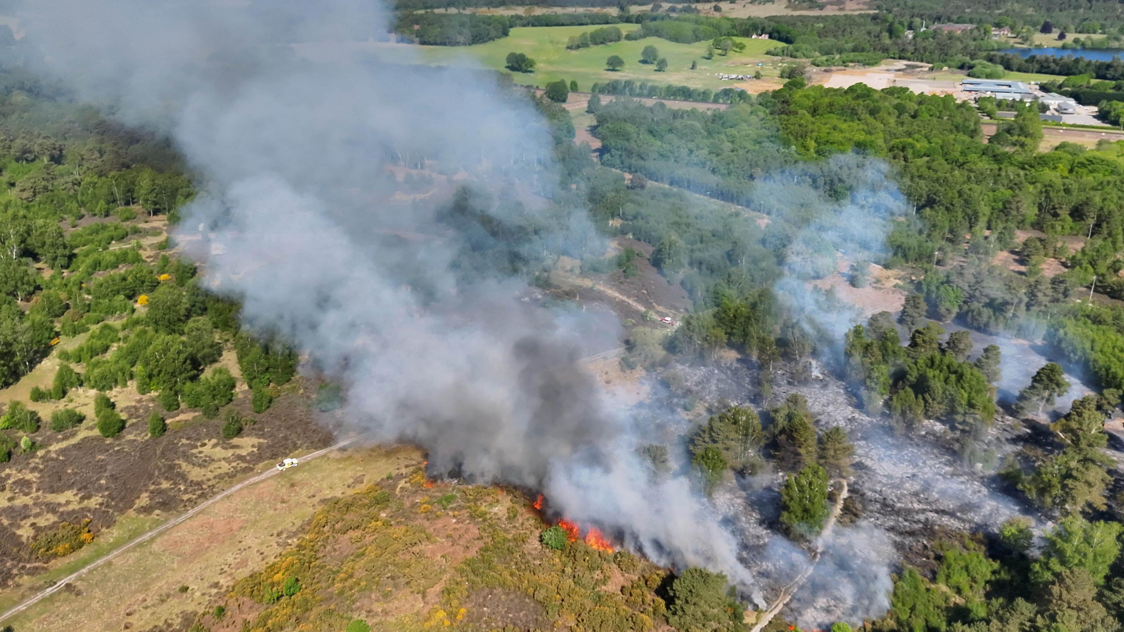 White and grey smoke rising over the countryside. The smoke comes from flames and charred ground.