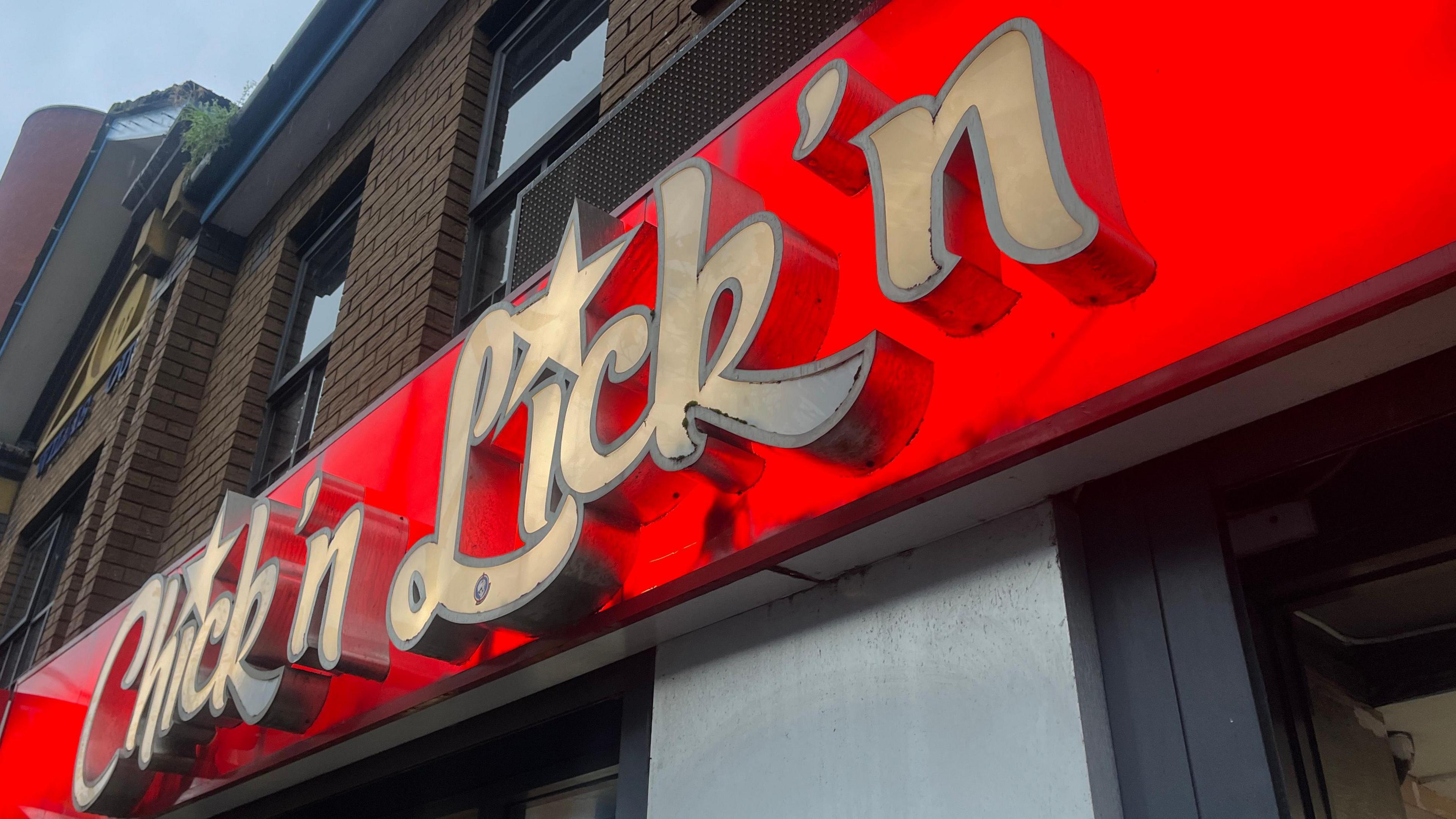 A red and white illuminated shop-front sign which reads Chick'n Lick'n