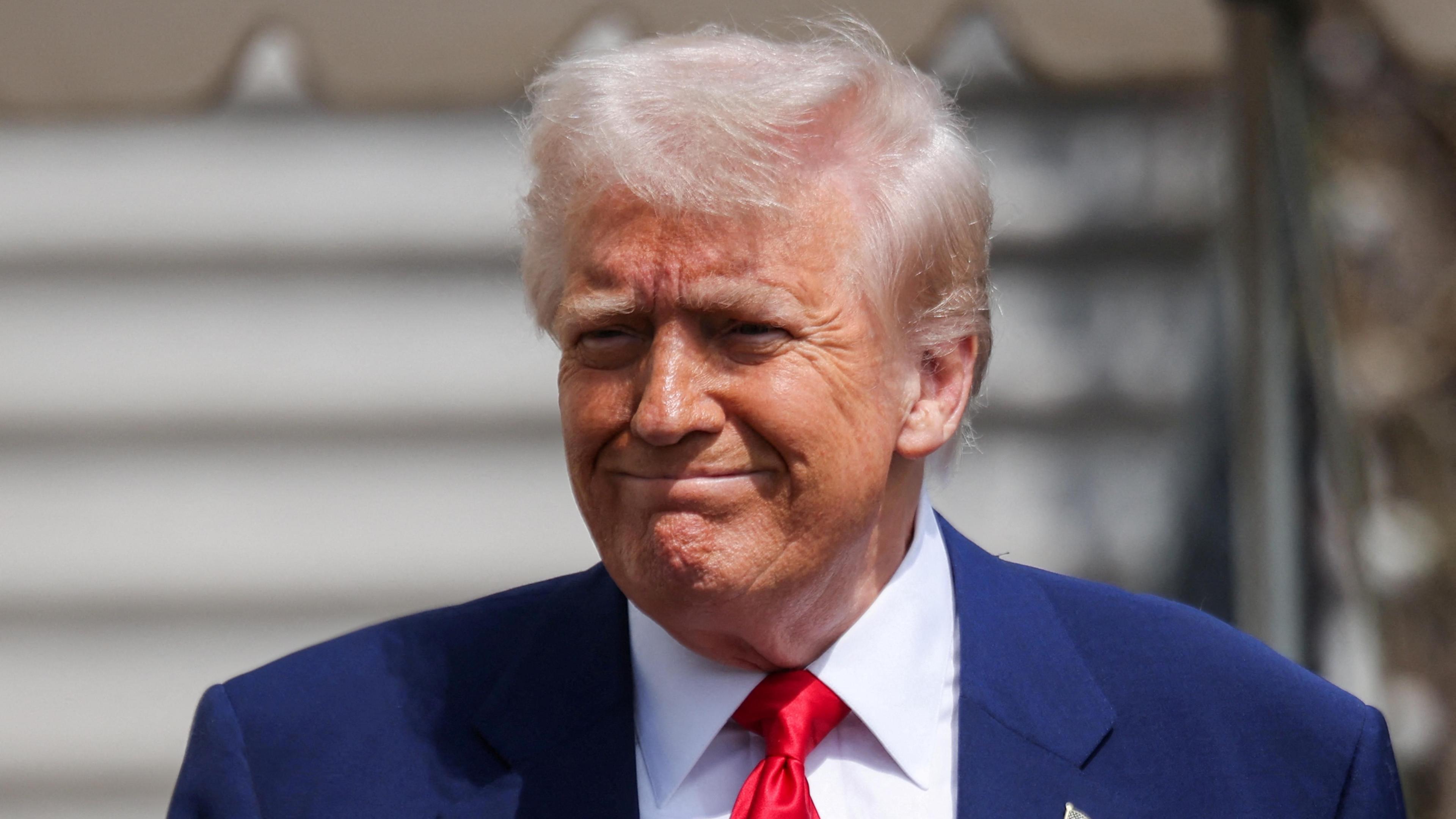 U.S. President Donald Trump reacts with pursed lips and furrowed brow before boarding Marine One, while departing the White House en route to Florida. He wears a blue jacket, white shirt and red tie