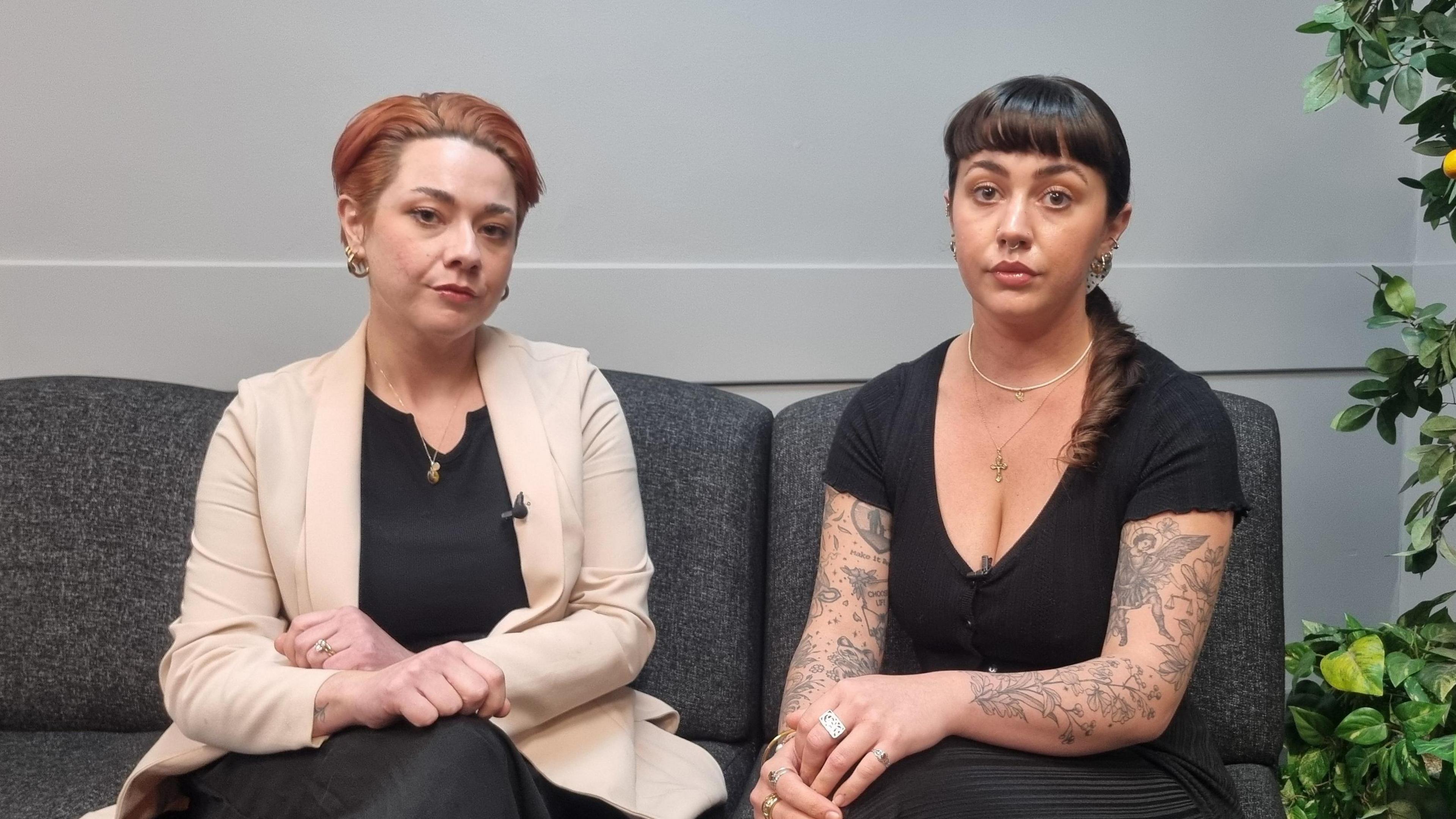 Liz Wilson and Catherine McSherry sitting on a sofa - Liz has short red hair - wearing a black top and cream blazer. Catherine has brown hair in a ponytail with a fringe - wearing a black top. 