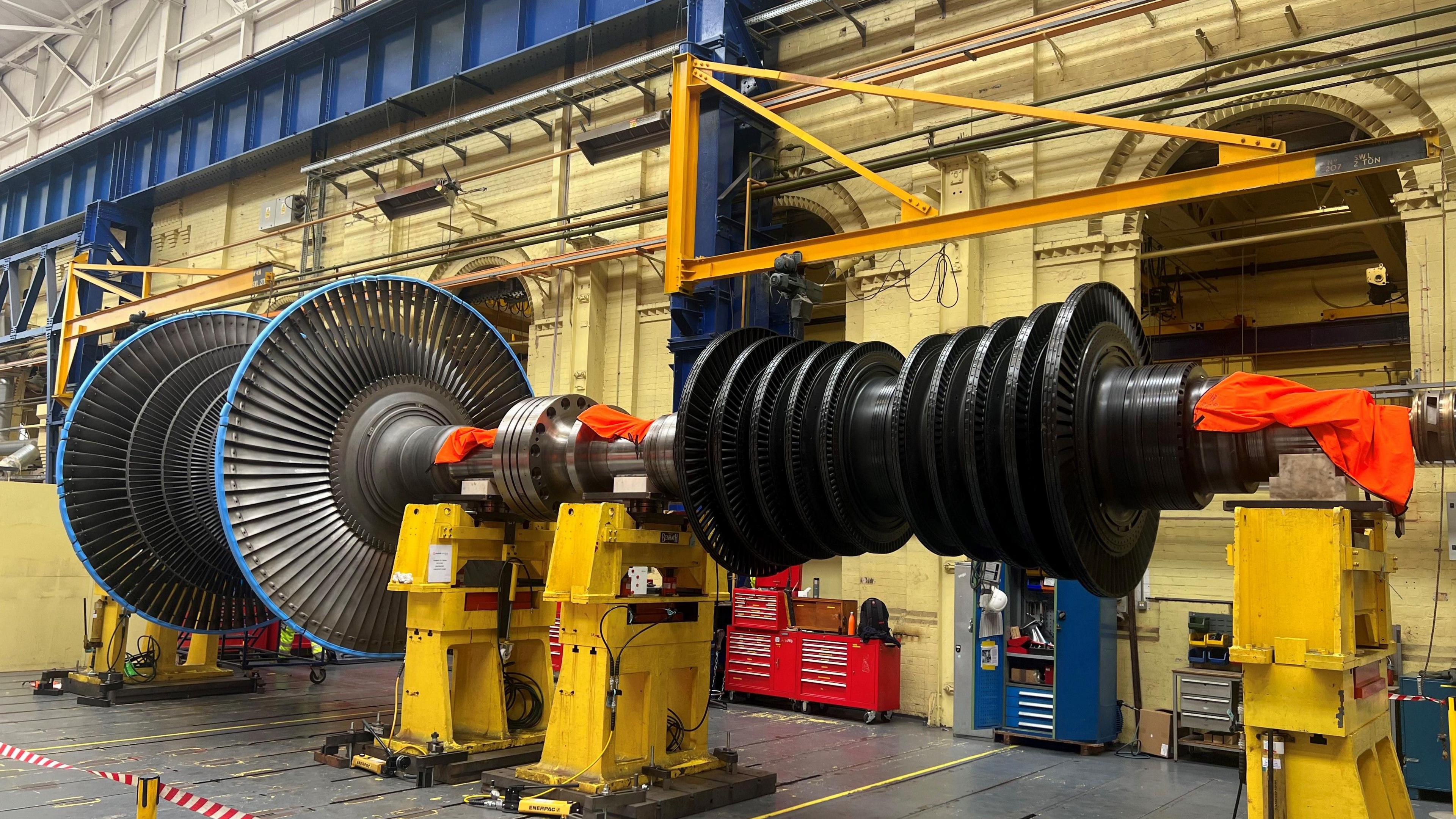 A general view of the nuclear station's giant rotor. It shows a large rotor within a large building and it is surrounded by other machinery.