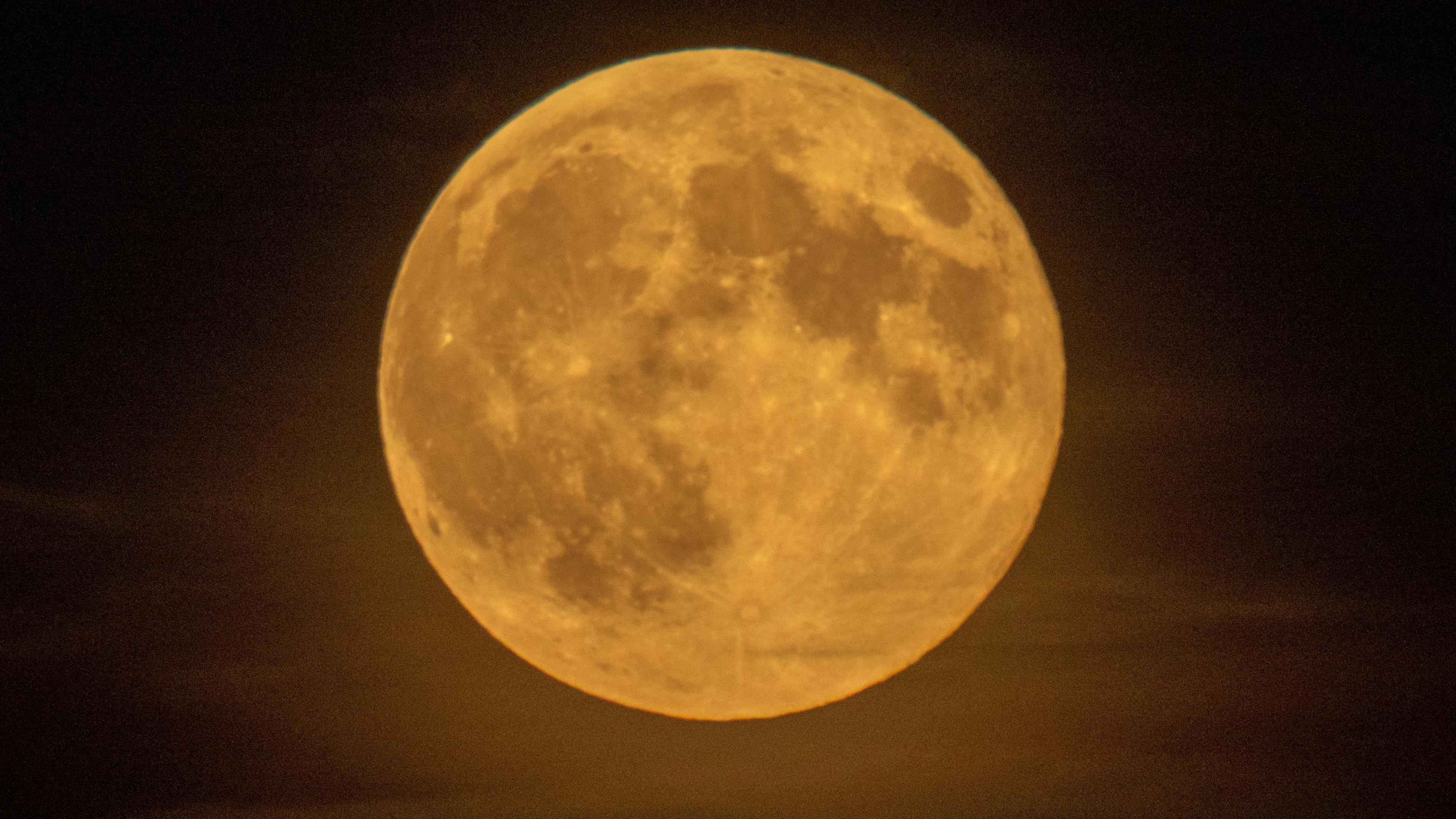 A bright orange moon close up to the image with brown craters on its surface