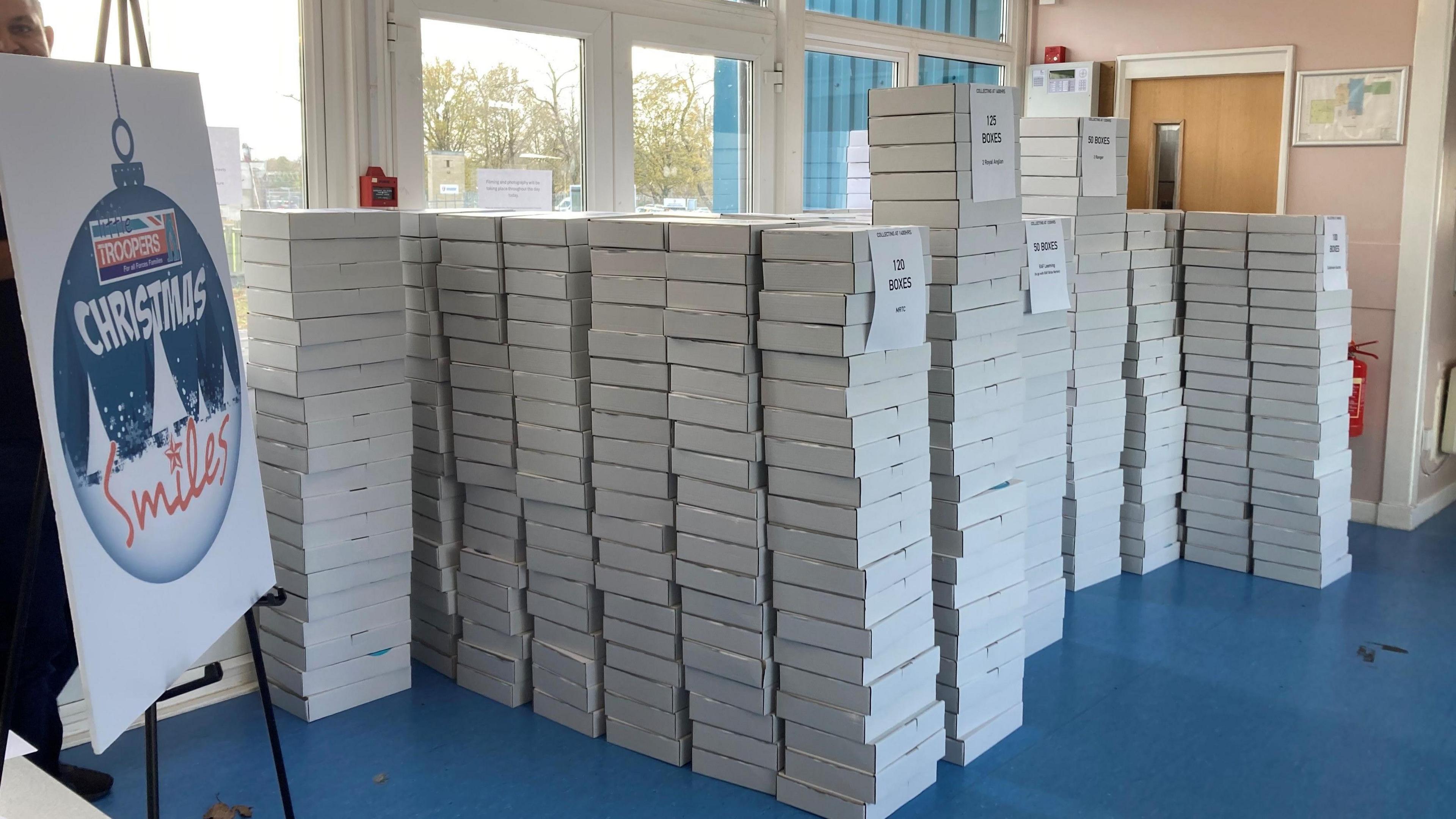 A pile of white boxes ready for delivery with a sign nearby which reads: "Little Troopers: Christmas Smiles".