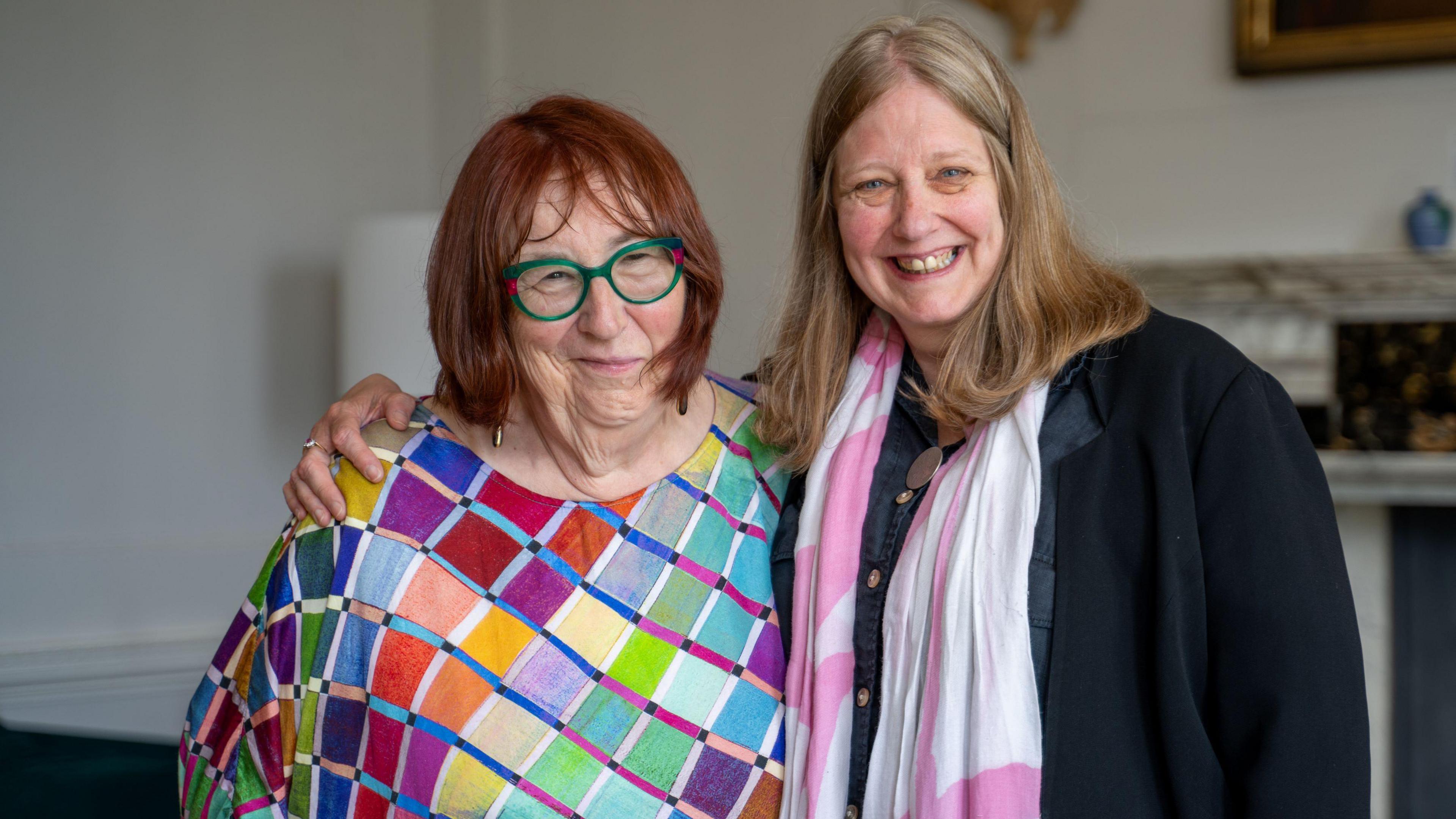 Rachel Carr, wearing a colourful dress with individual coloured squares, stands next to Ann Kennett, who is wearing a dark jacket and a pink and white scarf