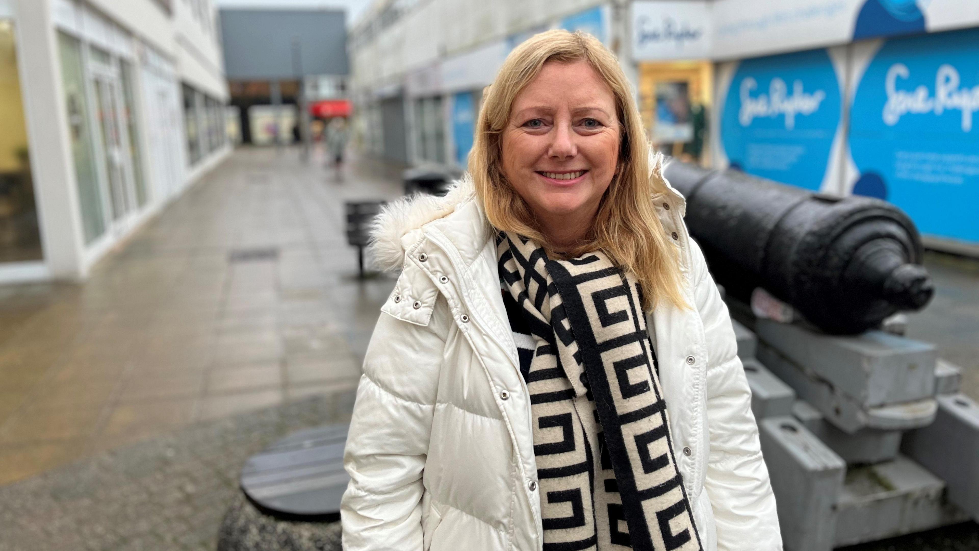 Antonia Harrison, cabinet member for thriving Waterlooville, stood in a white puffer jacket and a black and white scarf in the Waterlooville high street next to a cannon statue.