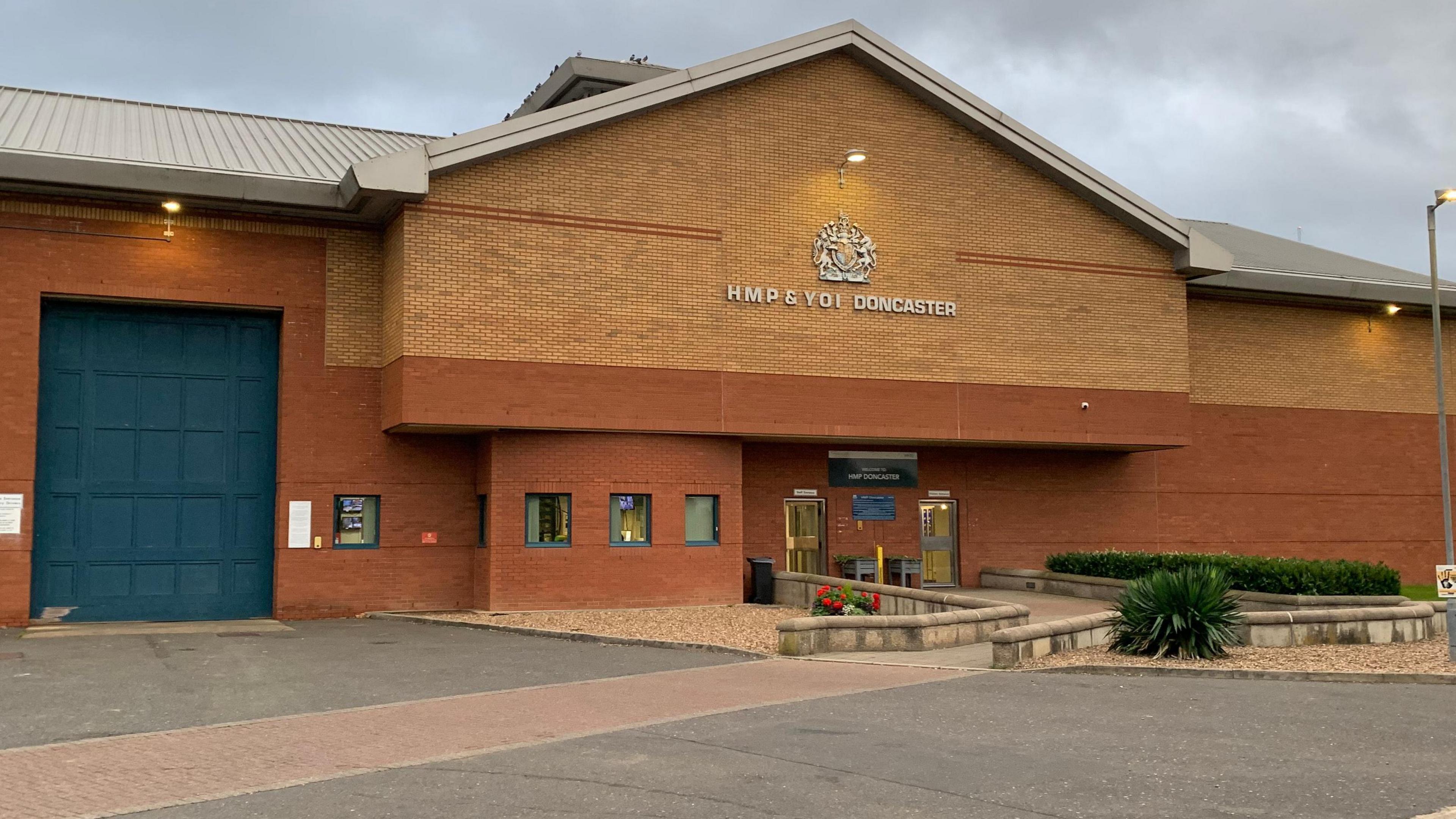 Brick-built HMP Doncaster with small all around entrance path and larger blue door for exits to the left of the image