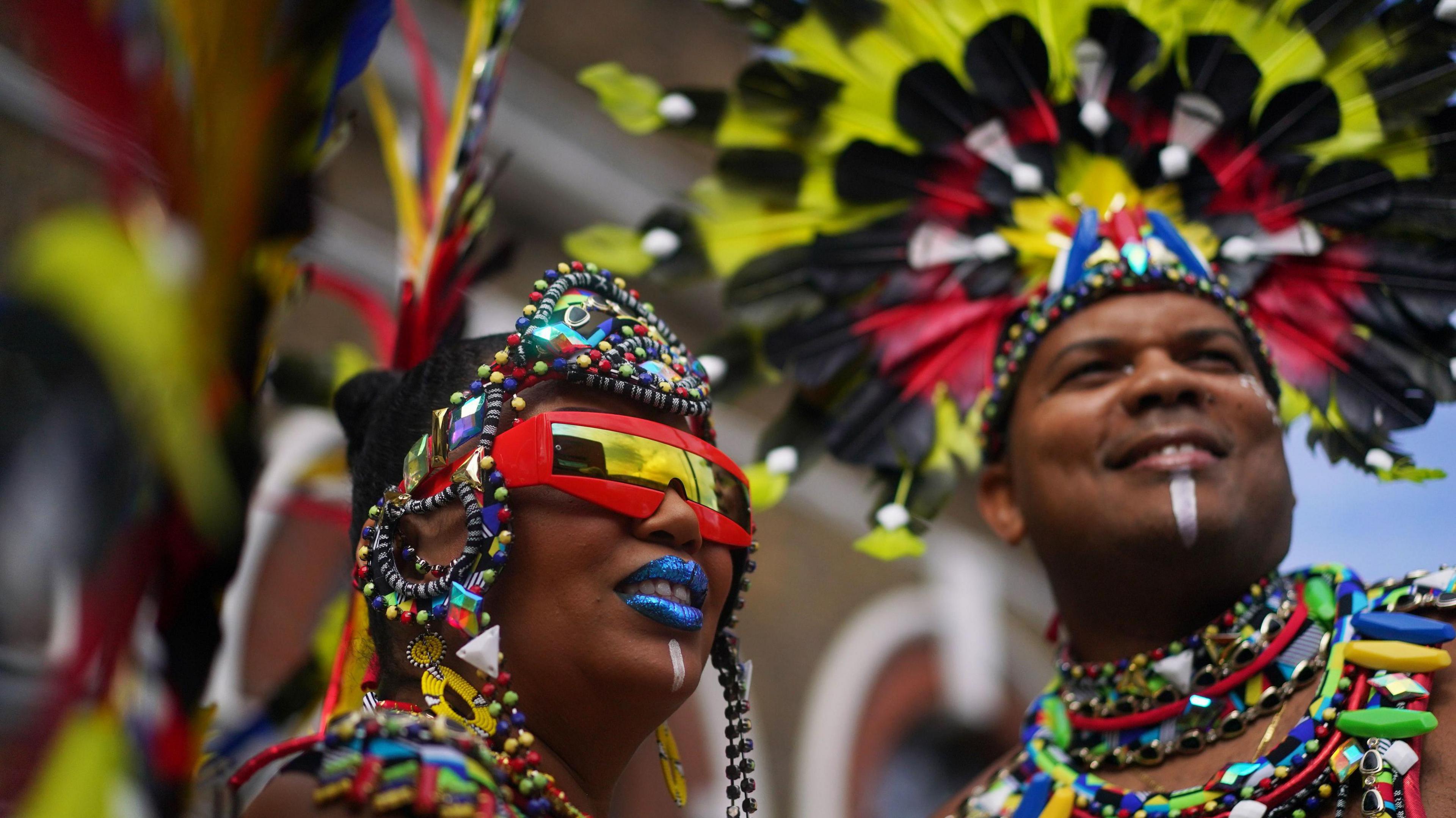 Head and shoulders shot of two dancers at Notting Hill carnival wearing colourful beaded headdresses and necklaces.