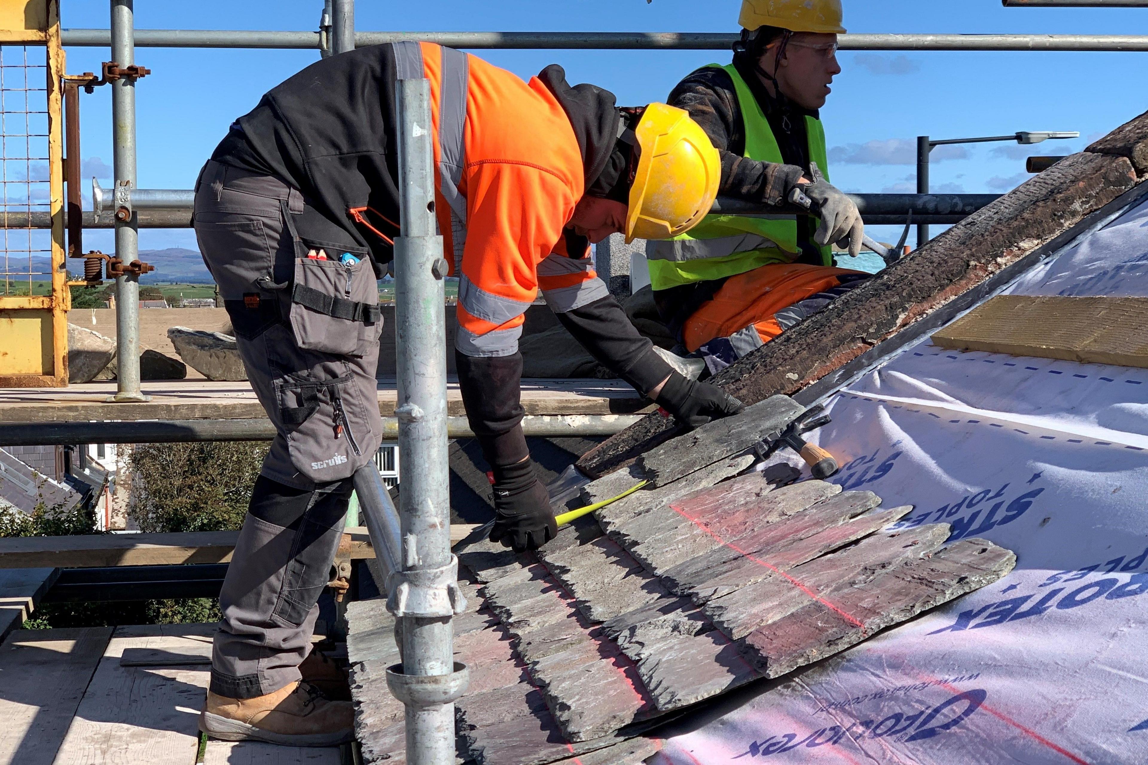 Two workers with yellow hard hats and high-viz tops lay down a slate roof