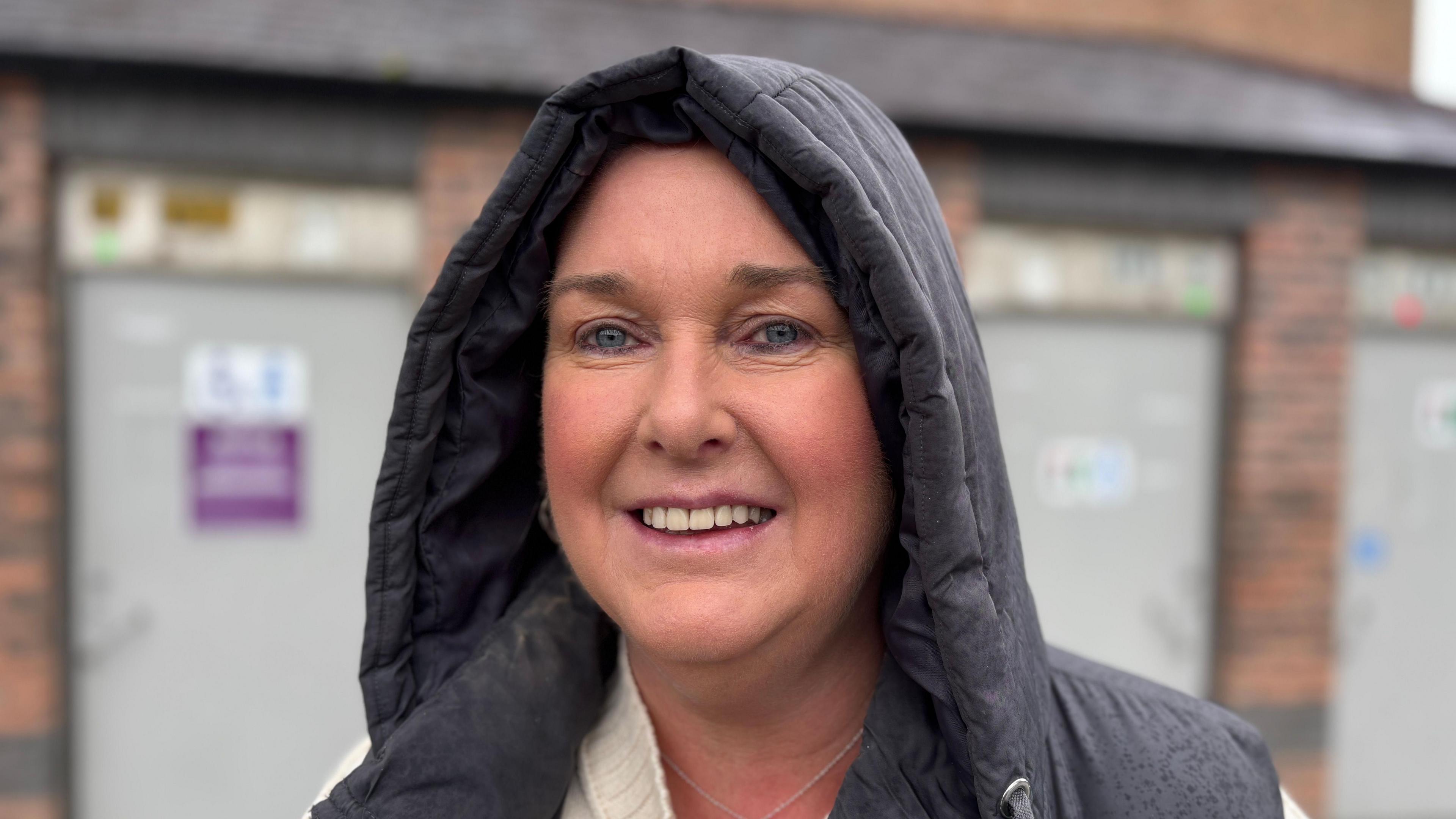 Mandy McClelland. She has blue eyes and wears a black hooded coat and a cream jumper.