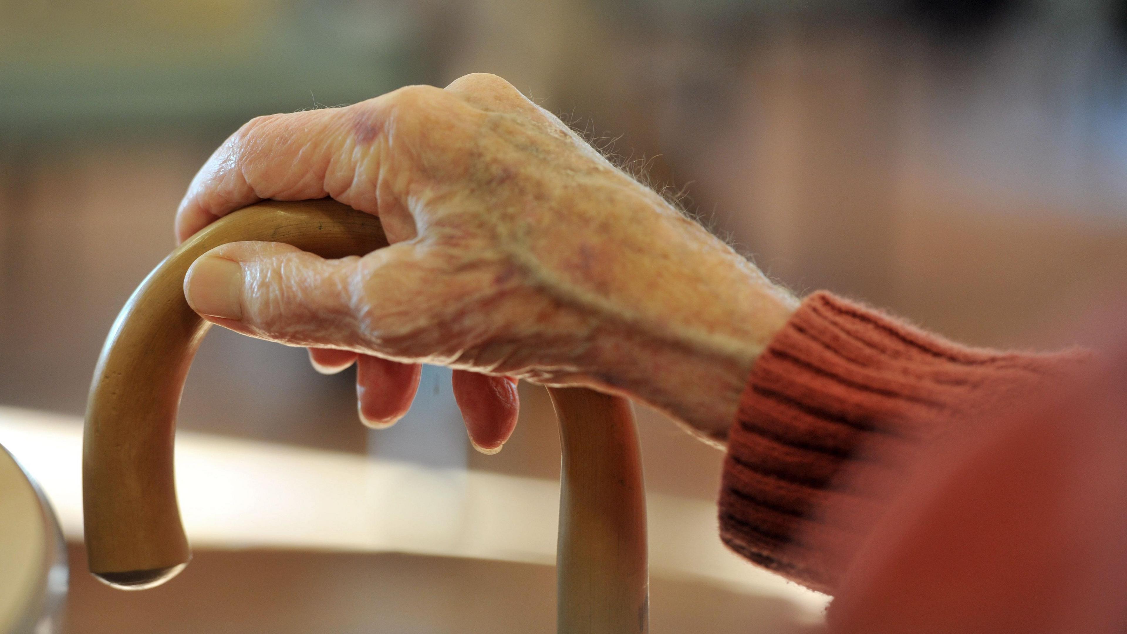 A stock image of an older person's hand holding a walking stick