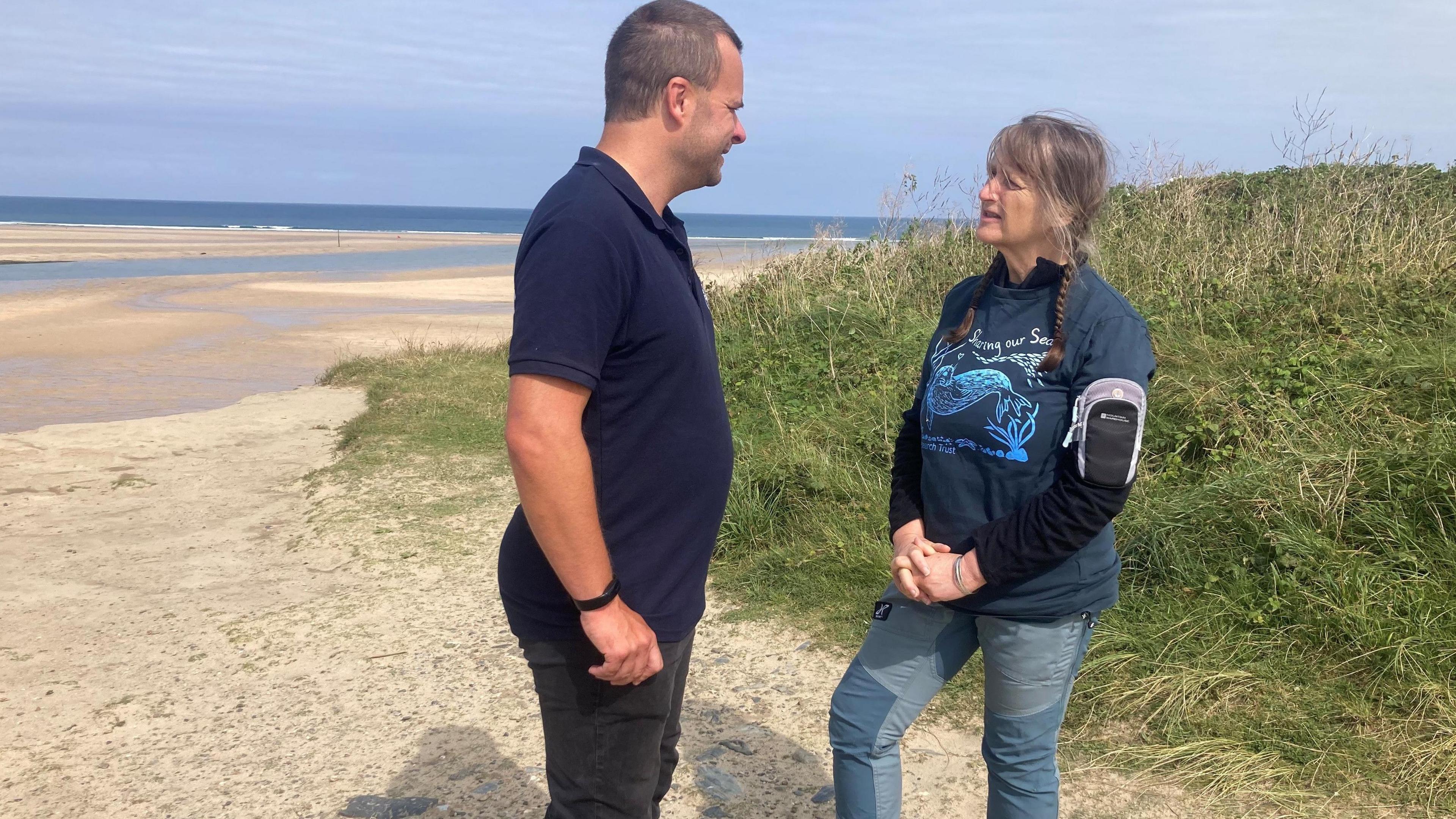 Sue Sayer from the Seal Research Trust and Dan Jarvis from the British Marine Life Rescue stand on a beach talking to one another