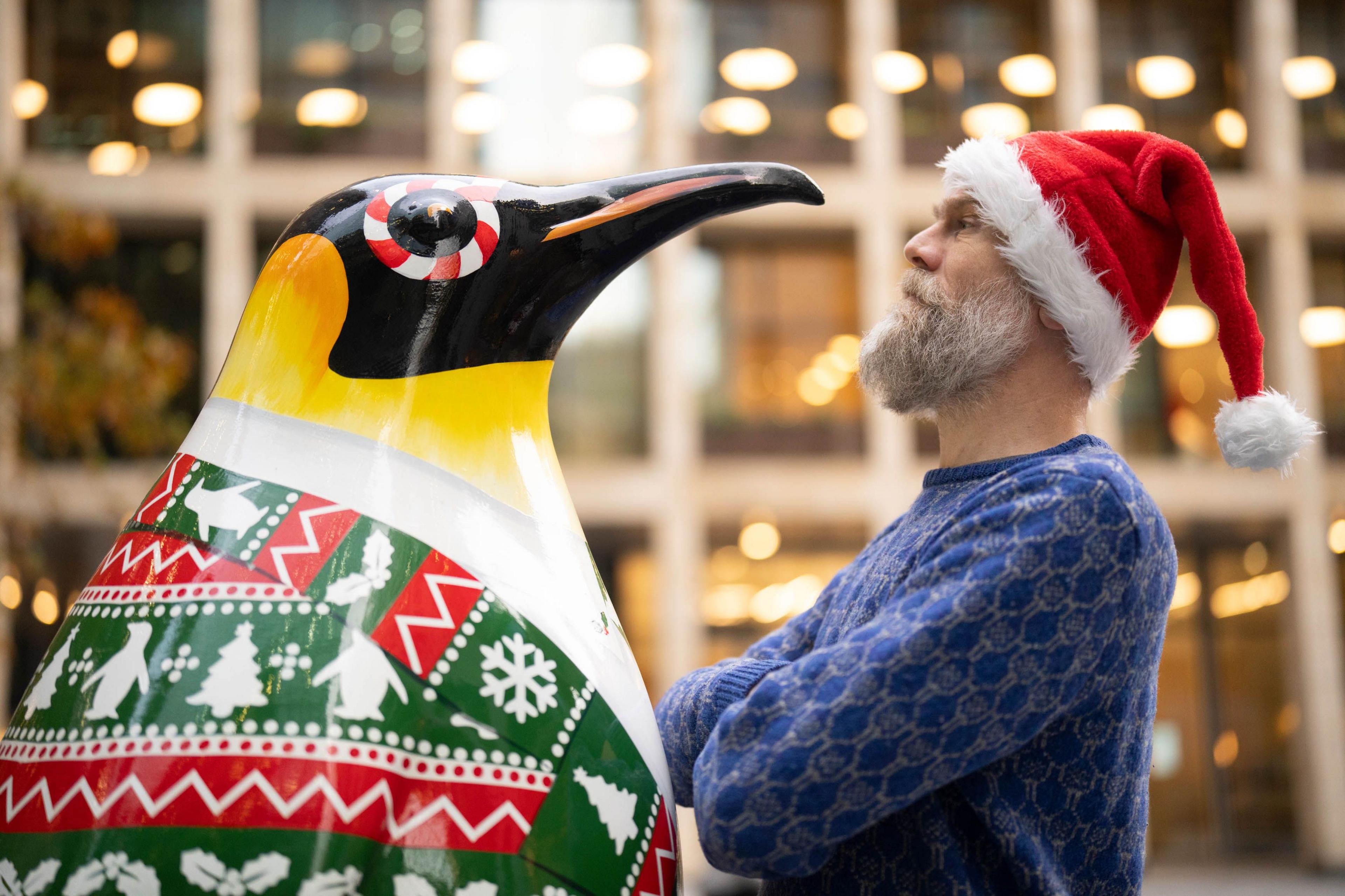 Author and Comedian Olaf Falafel (right) with a penguin statue in green and red festive suit with snowflakes and Christmas trees