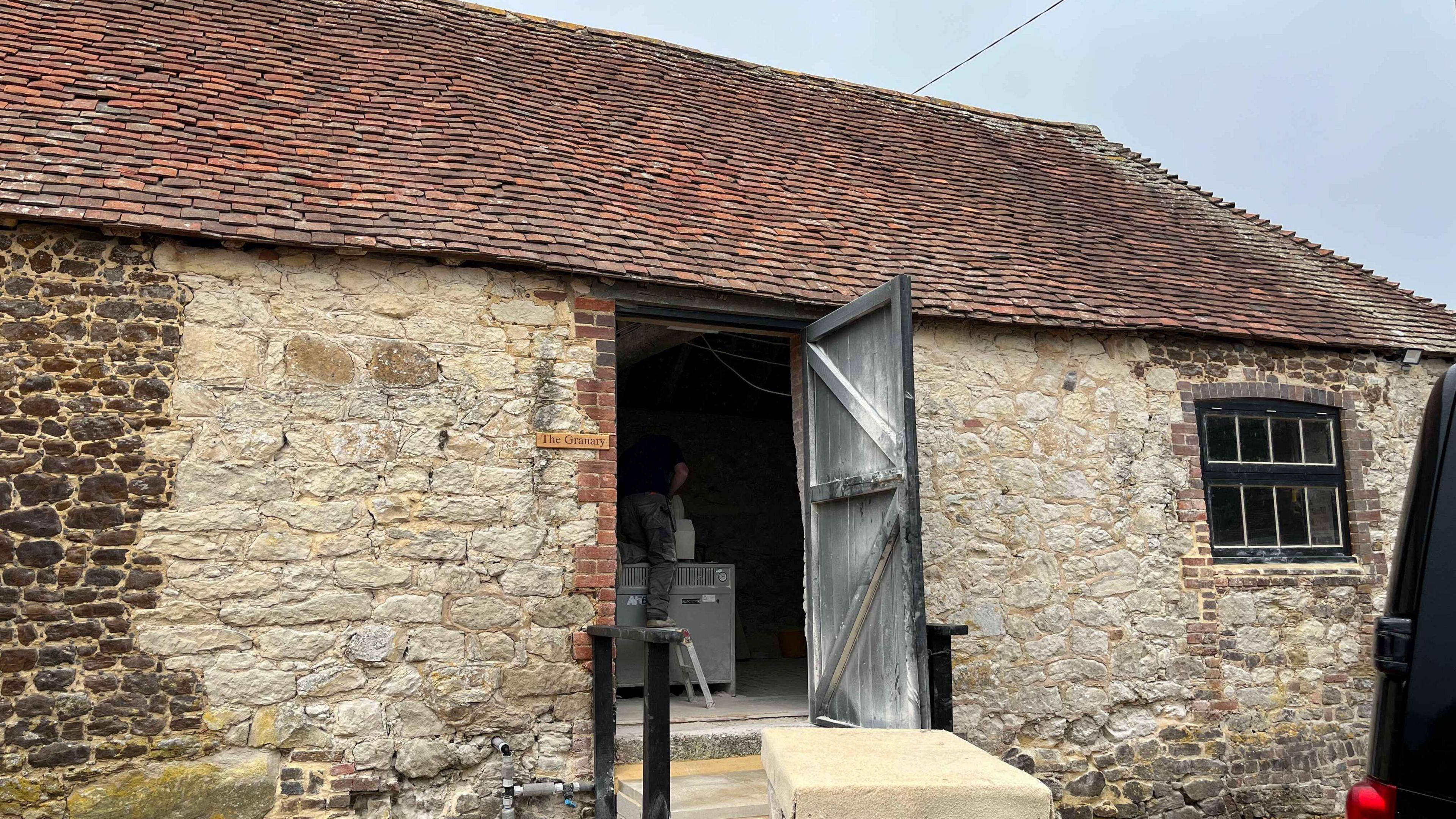 A barn with old bricks and red tiles with an open wooden door where the stonemasons work