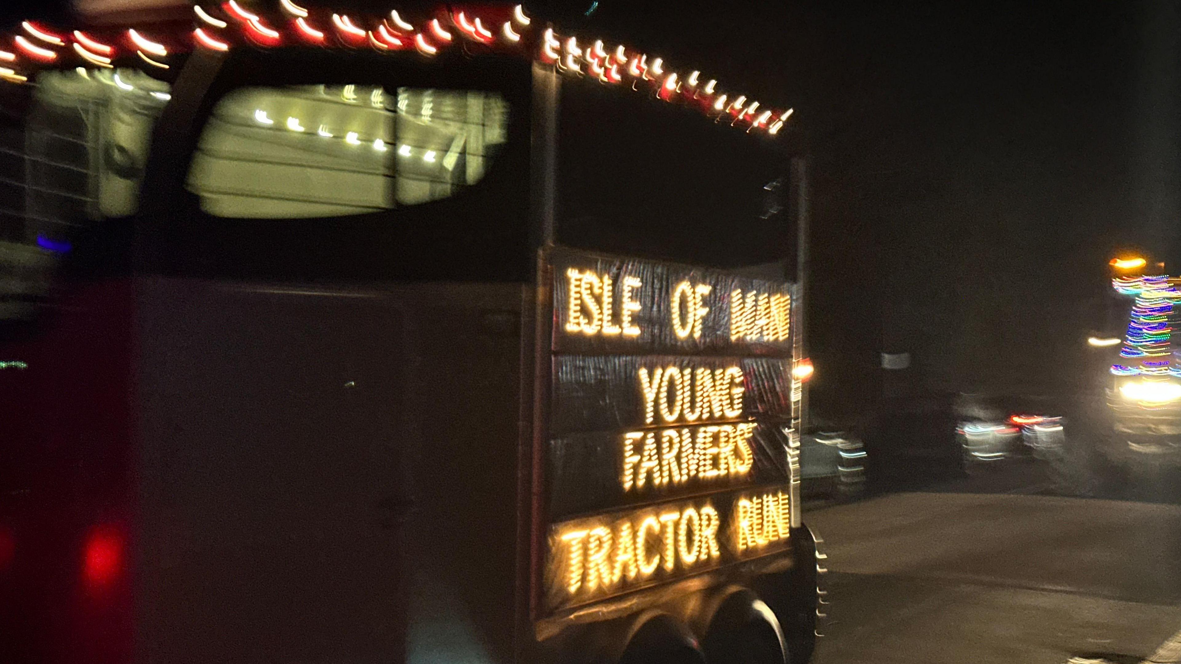 A trailer in the convoy with Isle of Man You Farmers Tractor Run in lights on the side.
