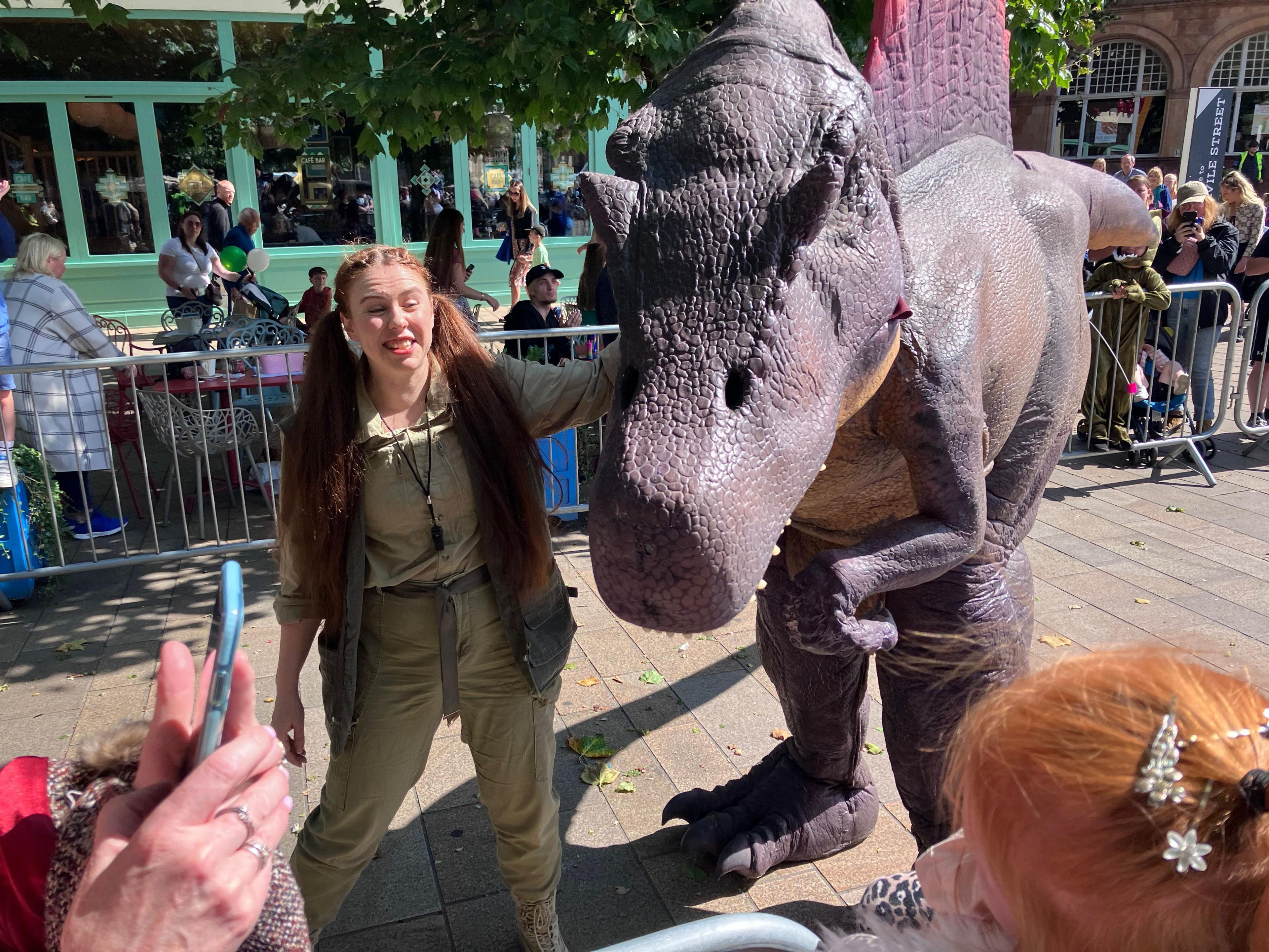 A female park ranger character talks about dinosaurs while posing with a "spinosaurus" for the crowd