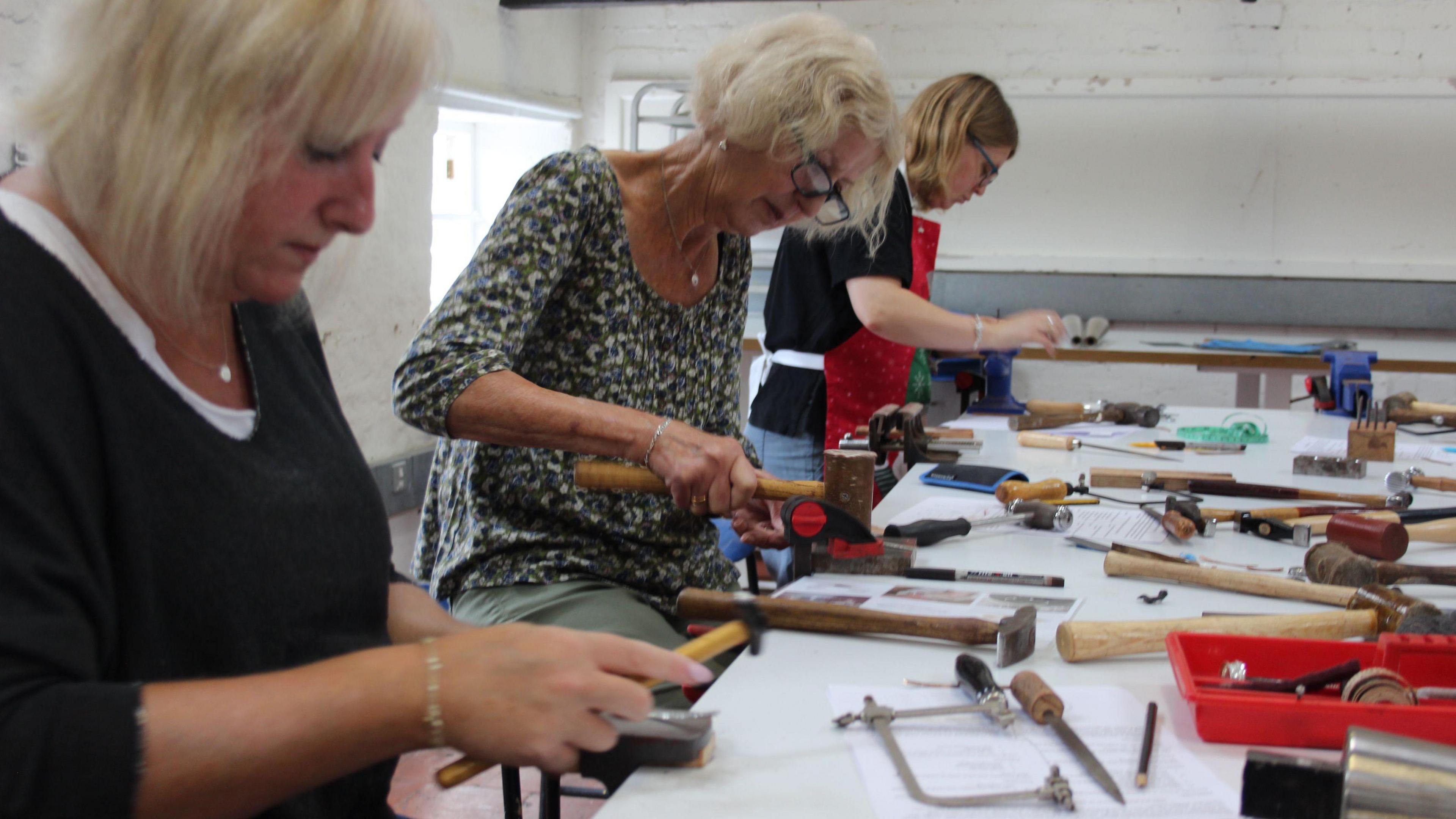 Three women making steel bangles in a workshop