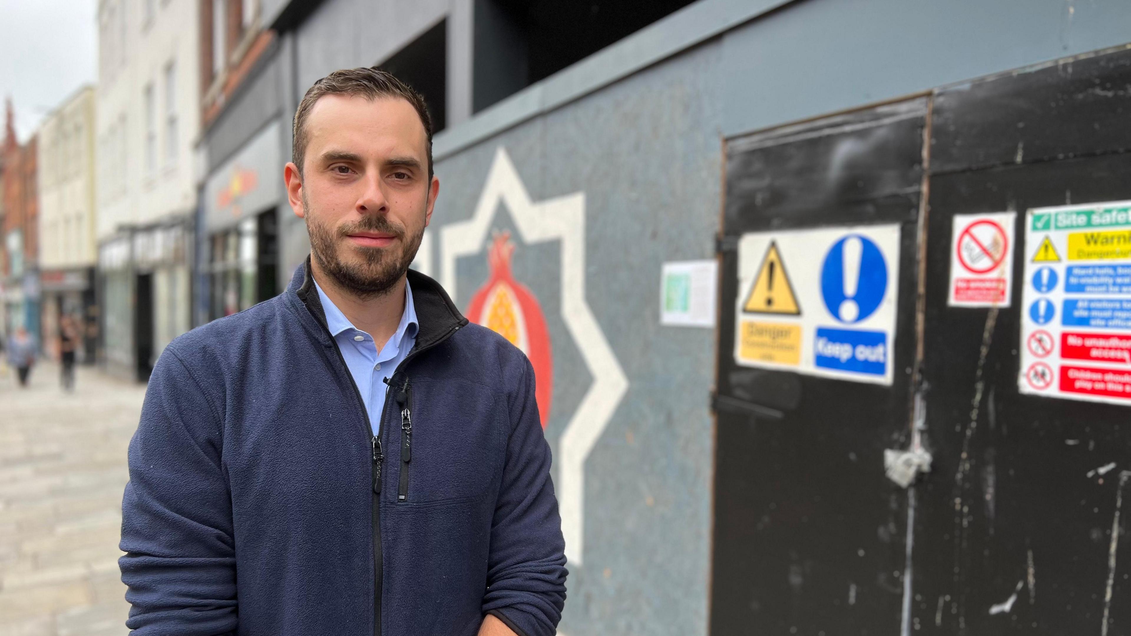 Luke Lutman, Chair of the Gloucester Chamber of Trade, stands in front of a big empty shop, which is now boarded up and painted