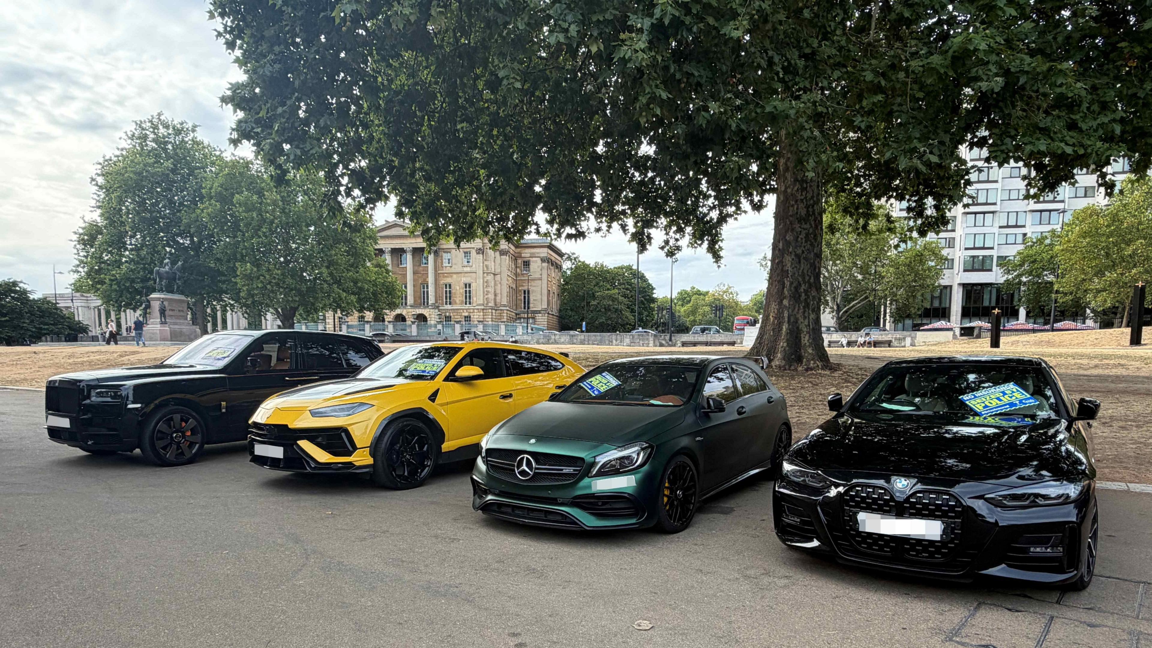 A Black Rolls-Royce, yellow Lamborghini, green Mercedes and black BMW parked side by side after being seized