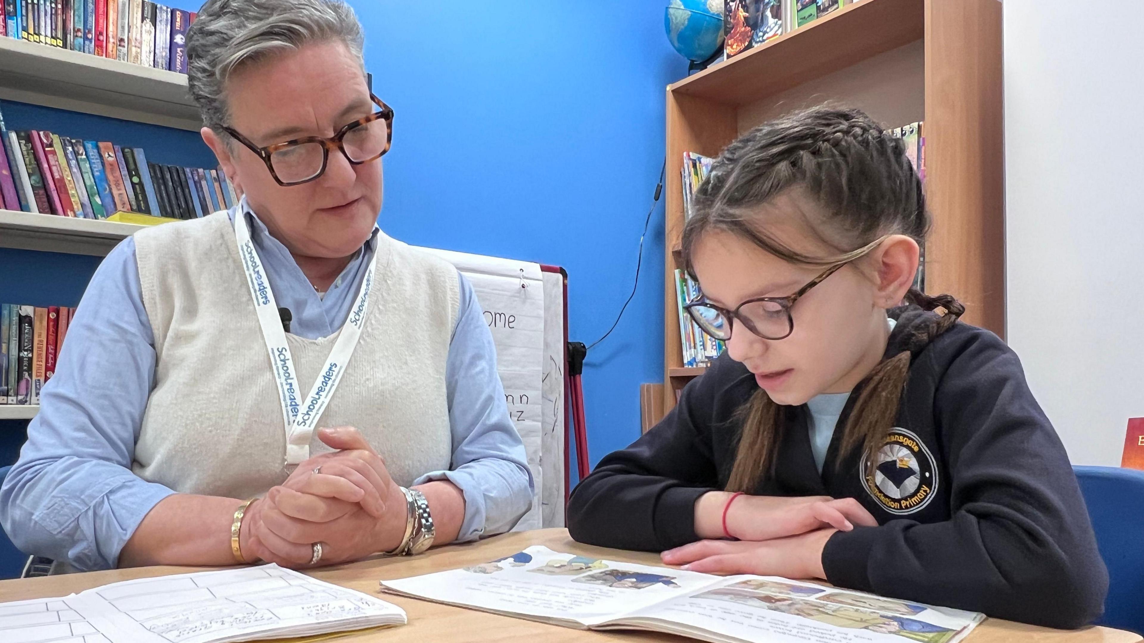 A woman with glasses looks at a book with a child from year three 