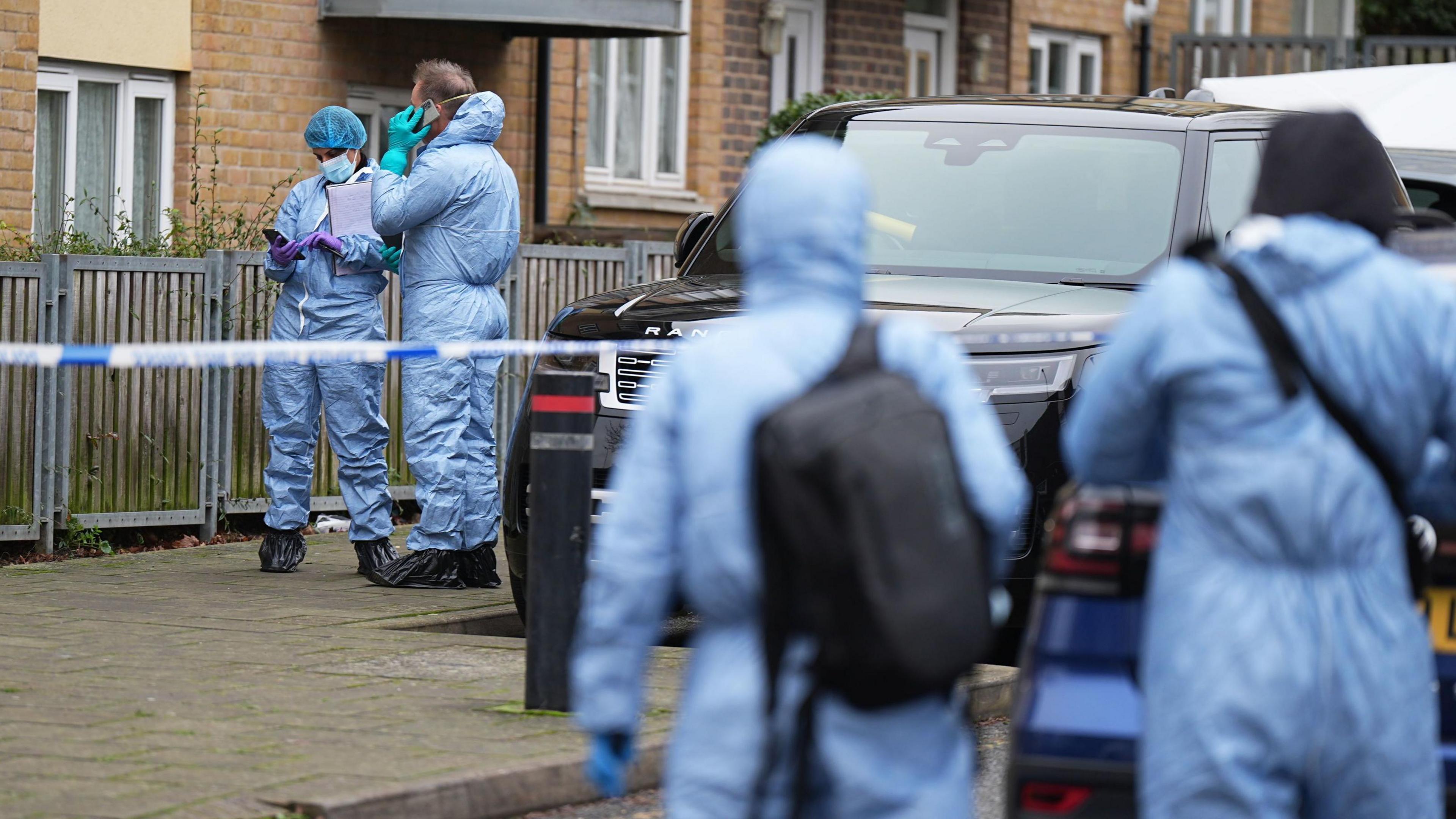 Forensics officers in blue overalls on the scene - a residential road