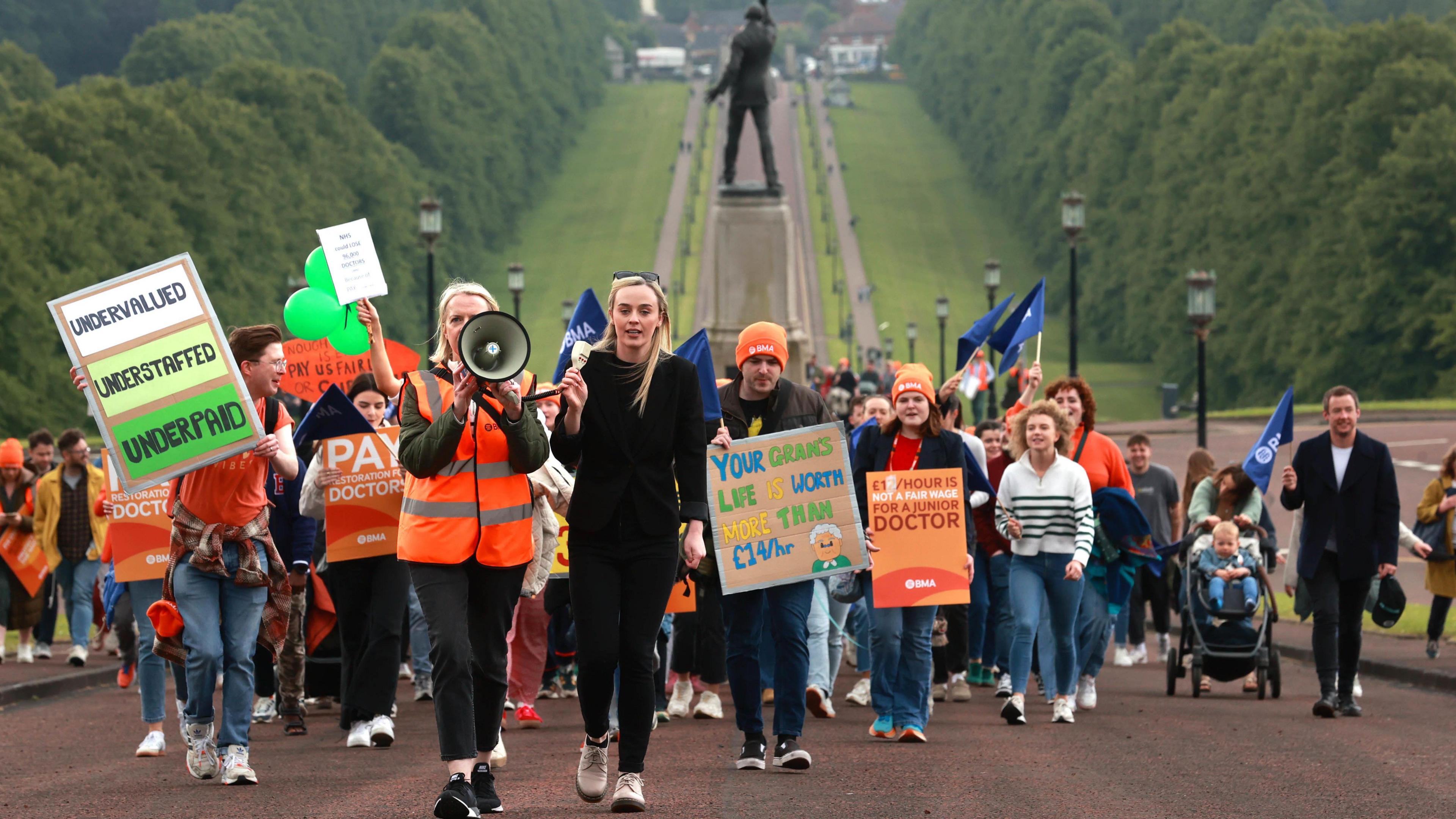 A crowd of junior doctors wearing orange reflective vests and holding signs walk up the hill at Stormont as they stage a protest in the midst of their walkout.