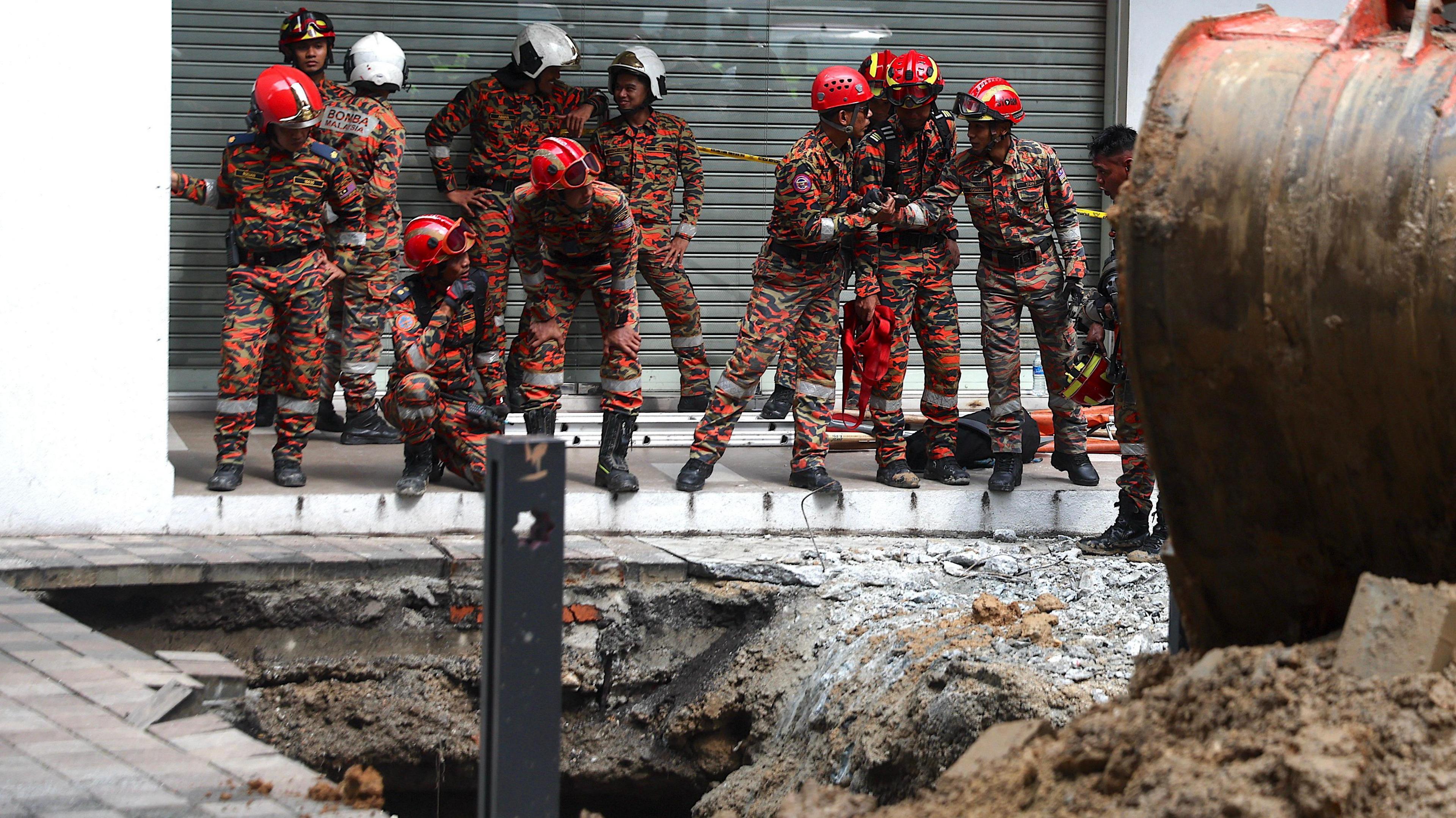 Malaysia Fire and Rescue Department officers inspect the site where a woman fell into an 8m deep sinkhole in Kuala Lumpur