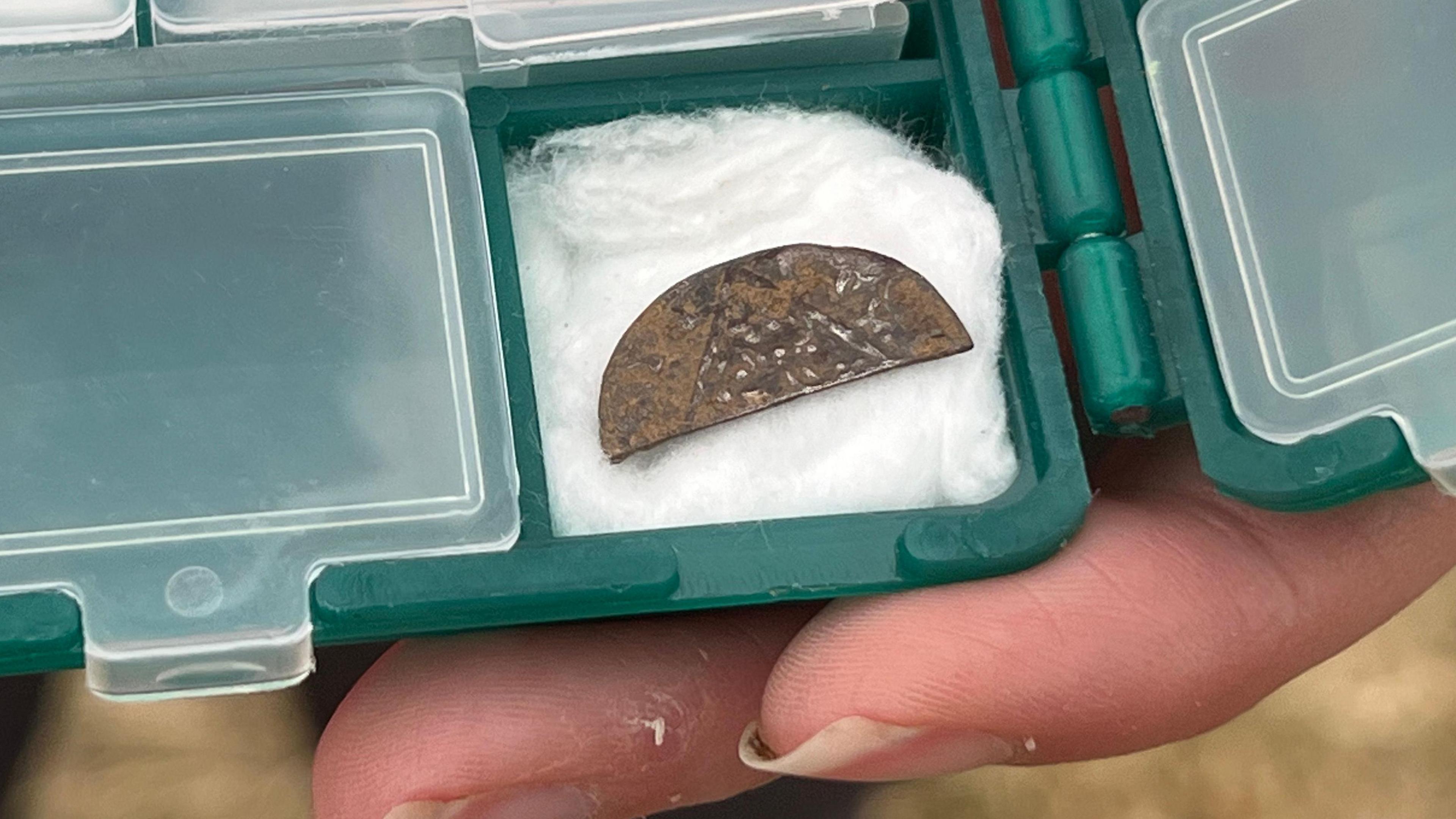 Half a coin or disc in a plastic container with small compartments being held up